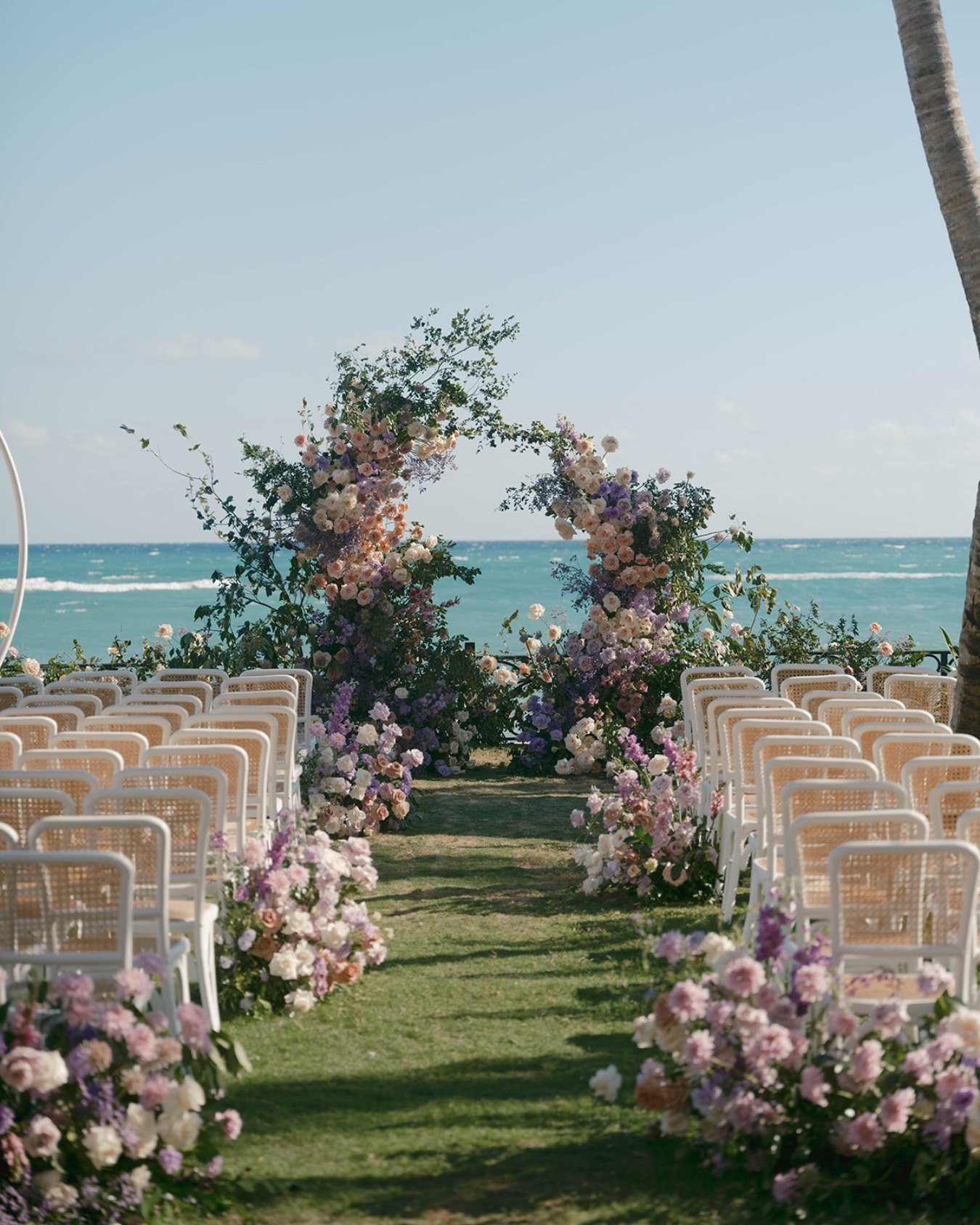 A beachside wedding setup with white chairs, floral arrangements, and an ocean view in the background.
