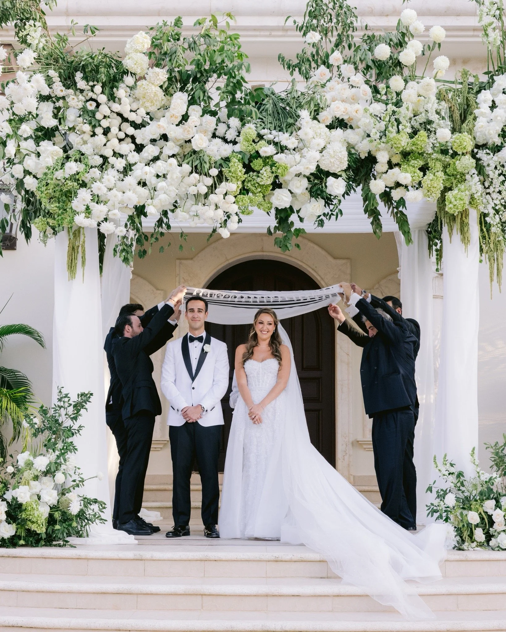 Bride and groom standing under a floral arch at their wedding ceremony.