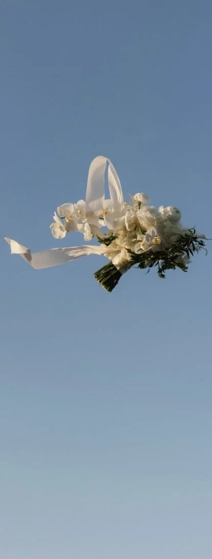 A white bridal bouquet with ribbon, floating against a blue sky background.
