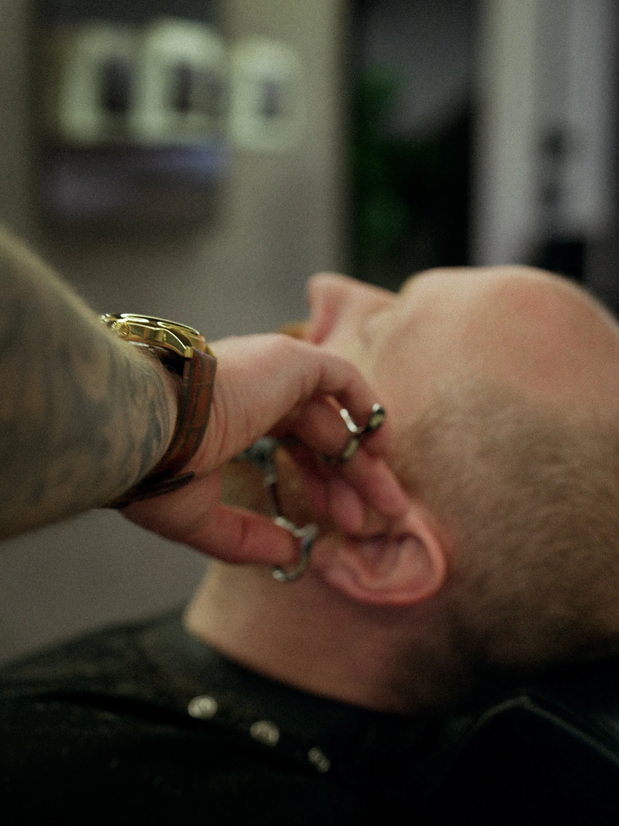 A person with tattoos has a hand on a man's face while he is lying down, and they are in a room with a thermostat on the wall in the background.