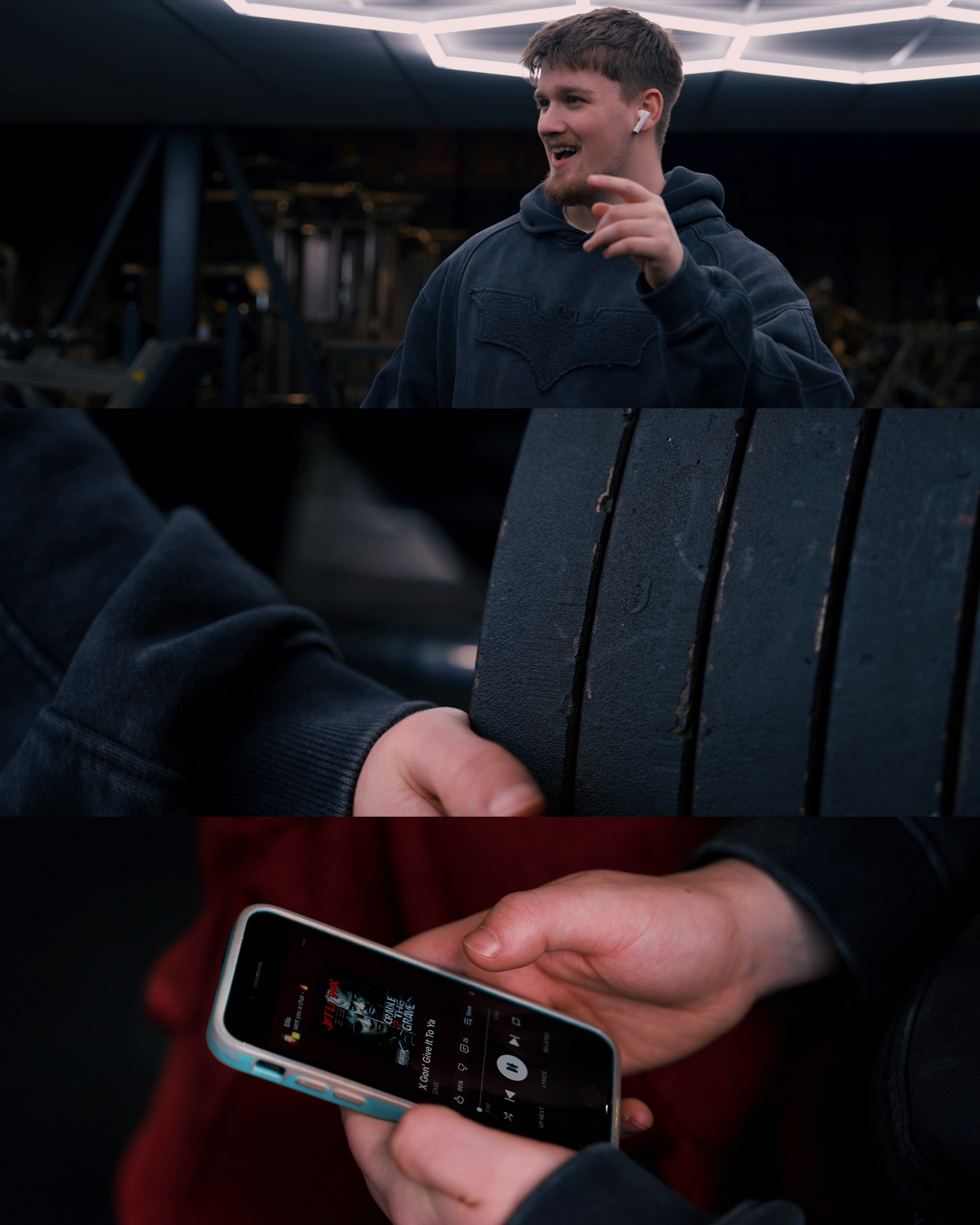 A young man smiling and pointing with his finger, wearing a hoodie and wireless earbuds, in a gym with dark lighting and geometric ceiling lights; close-up of a hand holding a tire, and another hand holding a smartphone playing a Netflix movie.