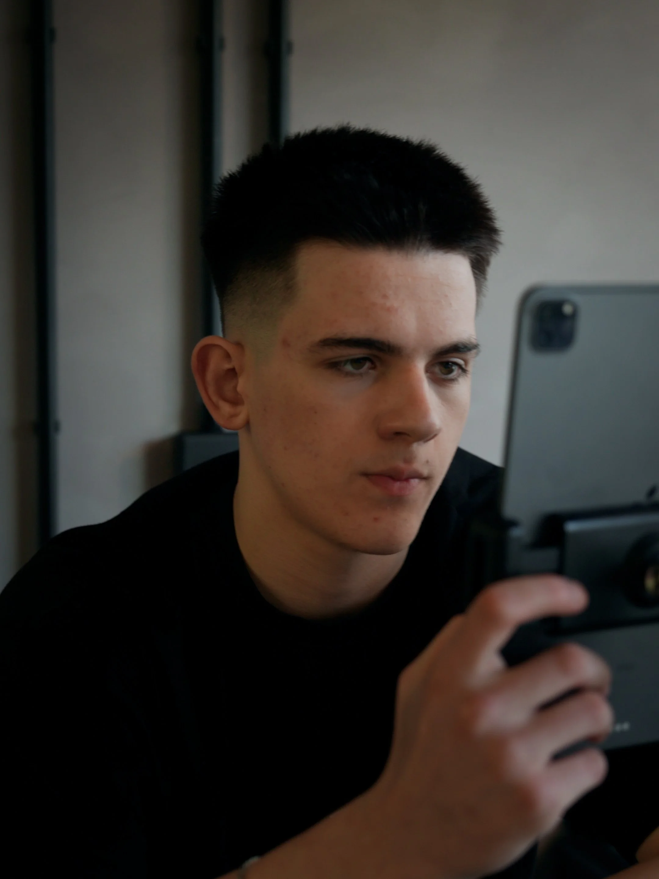 Young man with dark hair looking at a smartphone, wearing a black shirt in an indoor setting.