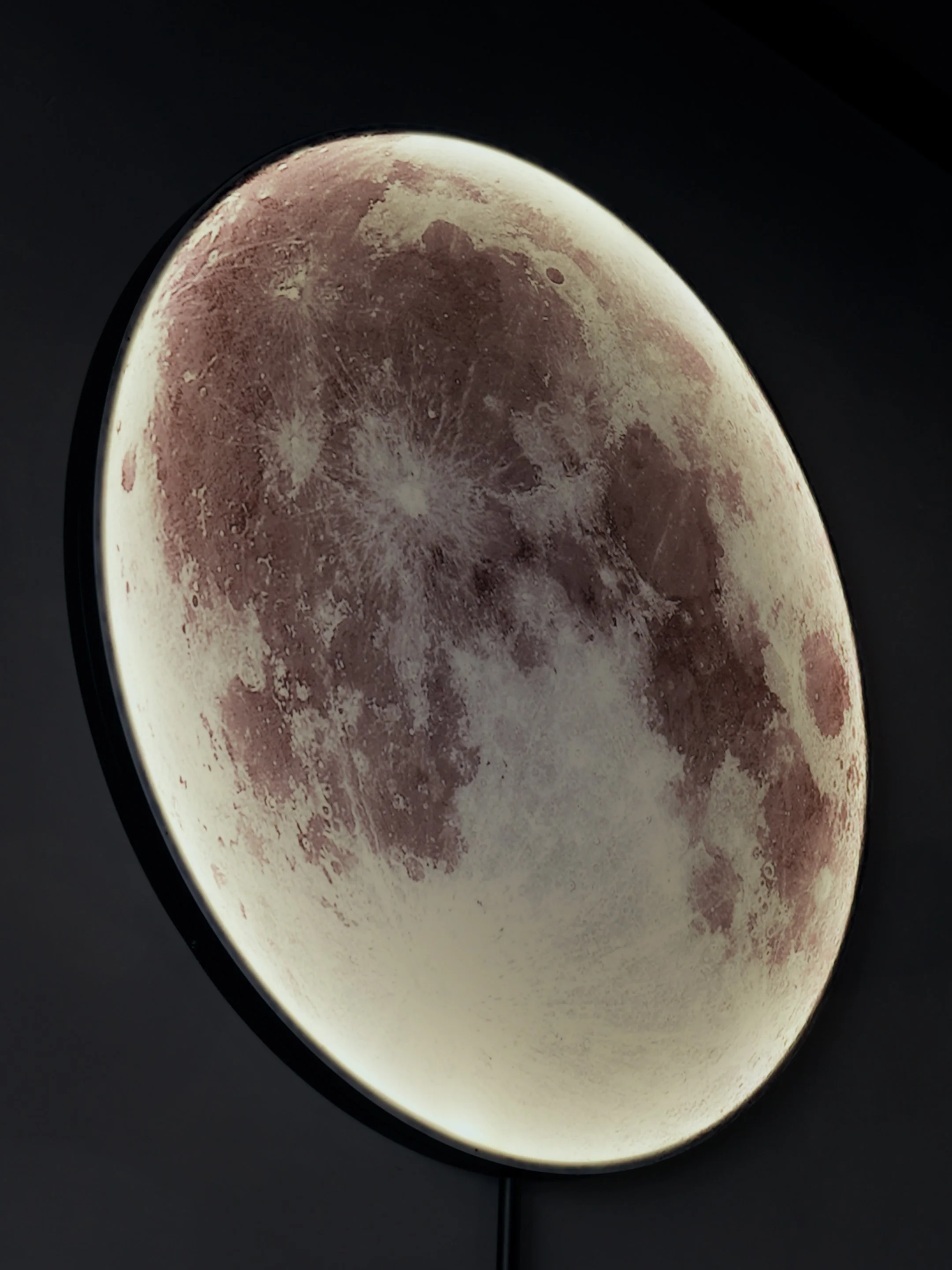 Close-up of a circular wall lamp designed to resemble the moon, emitting soft white light against a black background.