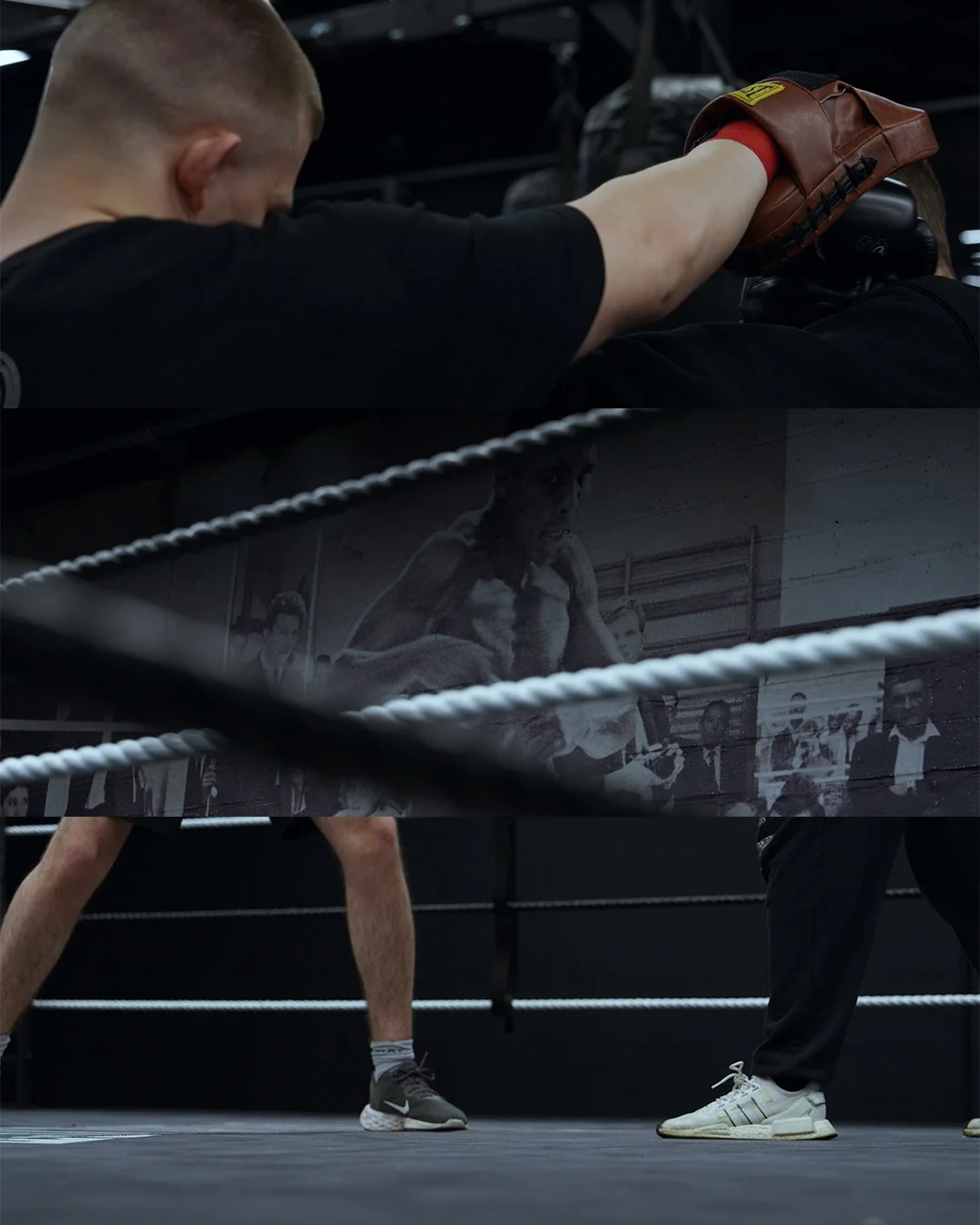 A boxing trainer or coach punches a punching bag inside a boxing gym. The gym has a congratulatory or historical photo on the wall showing a boxer in action.