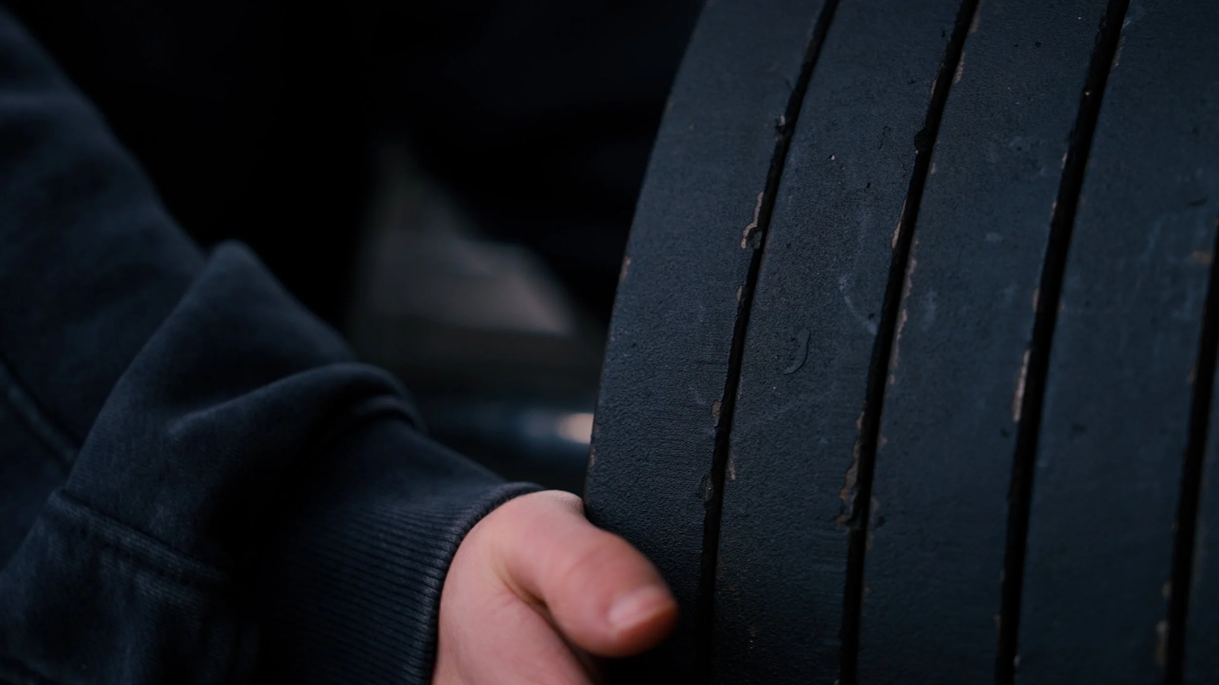 Person’s hand holding onto a black metal fence or barrier, wearing a dark jacket or sweatshirt.
