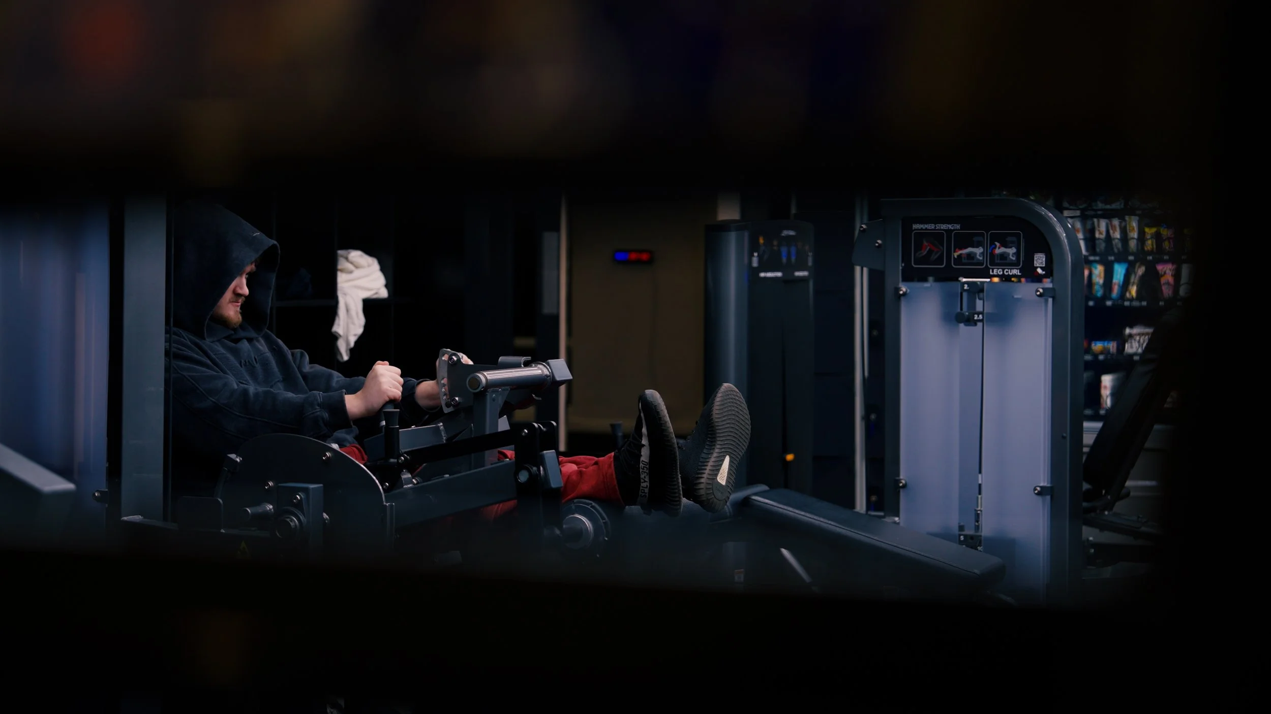 Person in a hoodie using a leg press exercise machine in a gym.