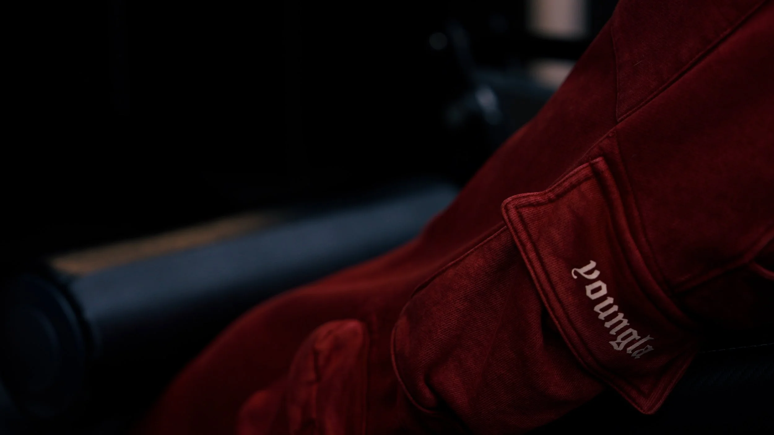 A person wearing a red jacket with a partially visible logo, sitting in a dark environment.