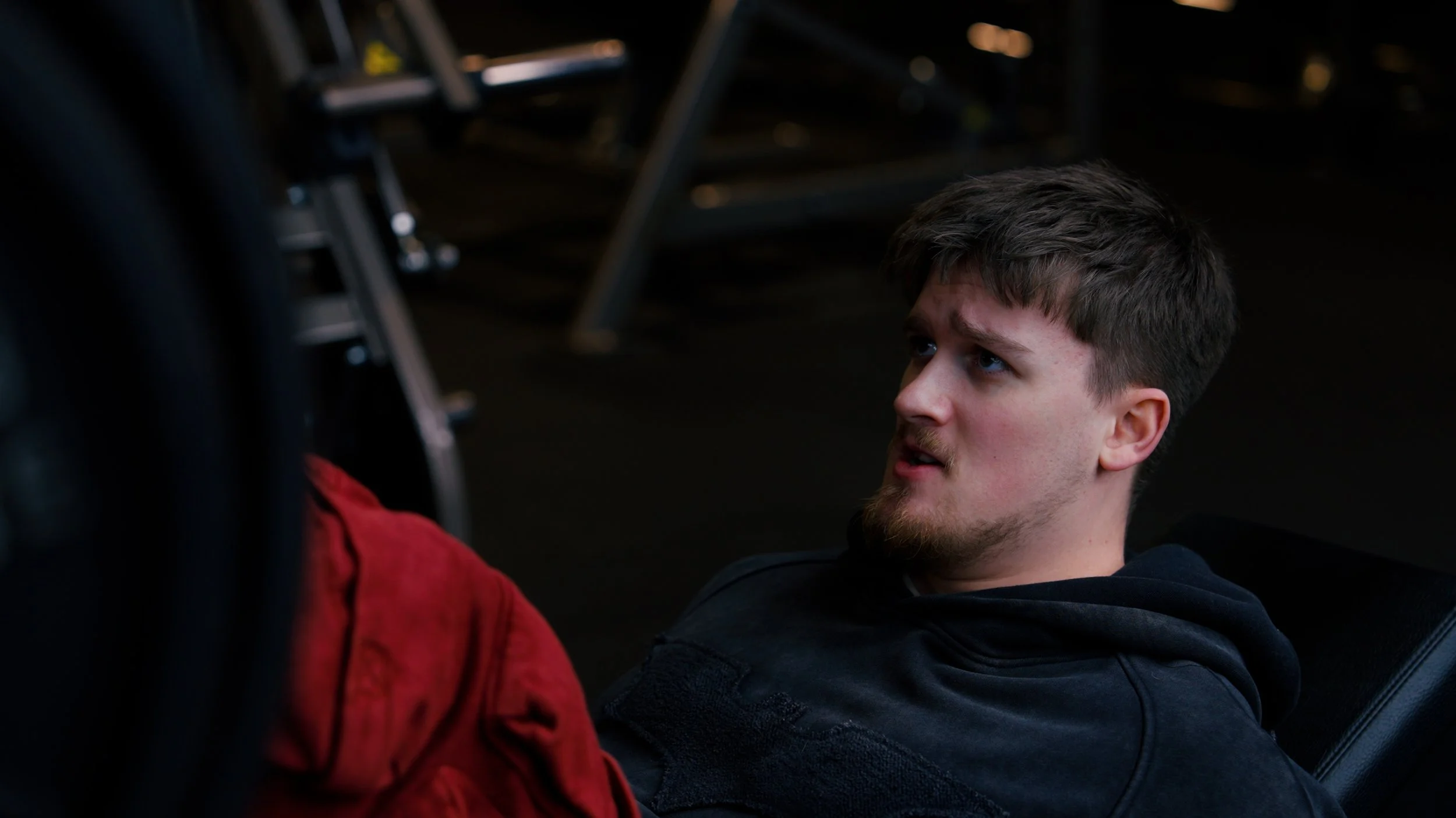 A man with short brown hair and a beard lying on the floor, looking up with a concerned expression.