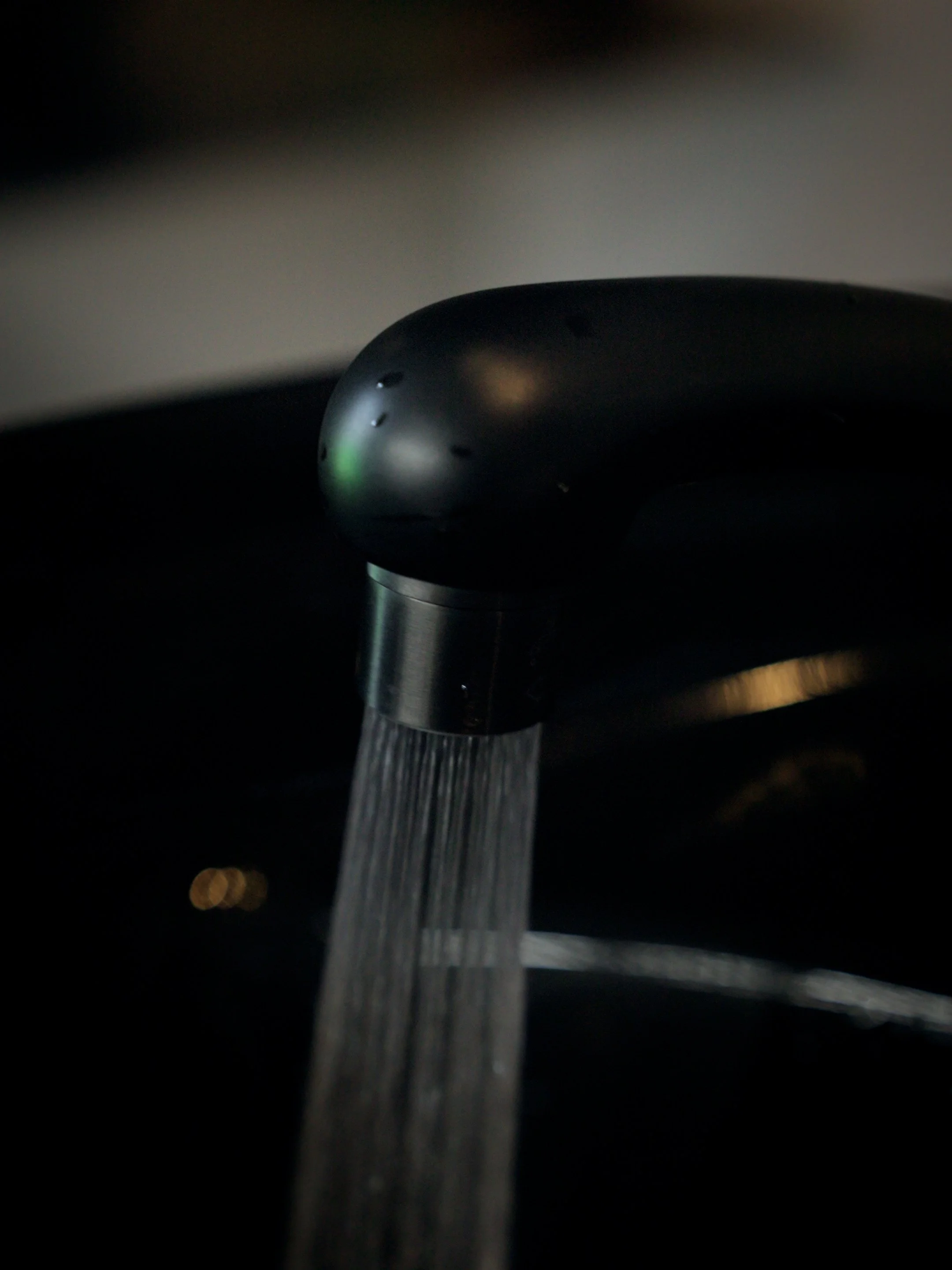 Close-up of a modern black kitchen faucet with water flowing from it, captured in low lighting.