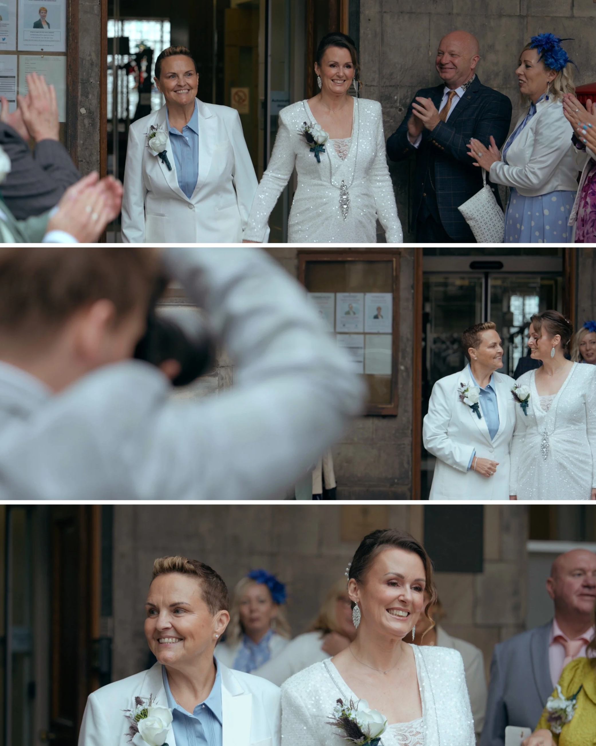 A procession of three women in white outfits, with two of them wearing white jackets and the middle one in a white dress, walking together at a wedding event. They are surrounded by clapping guests.