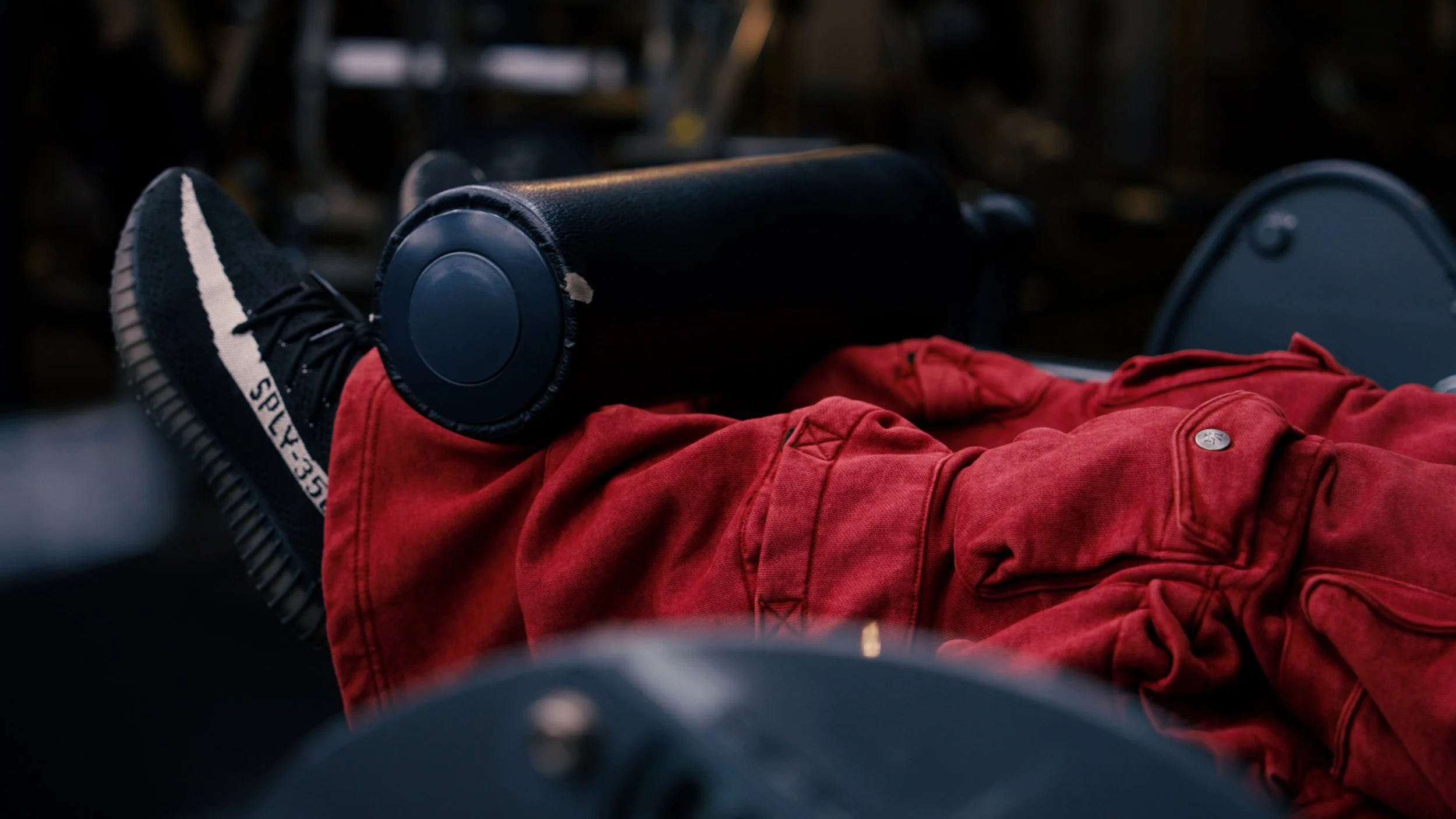 Person lying down on a chair or bench, wearing red pants and black sneakers, with headphones resting on their leg.