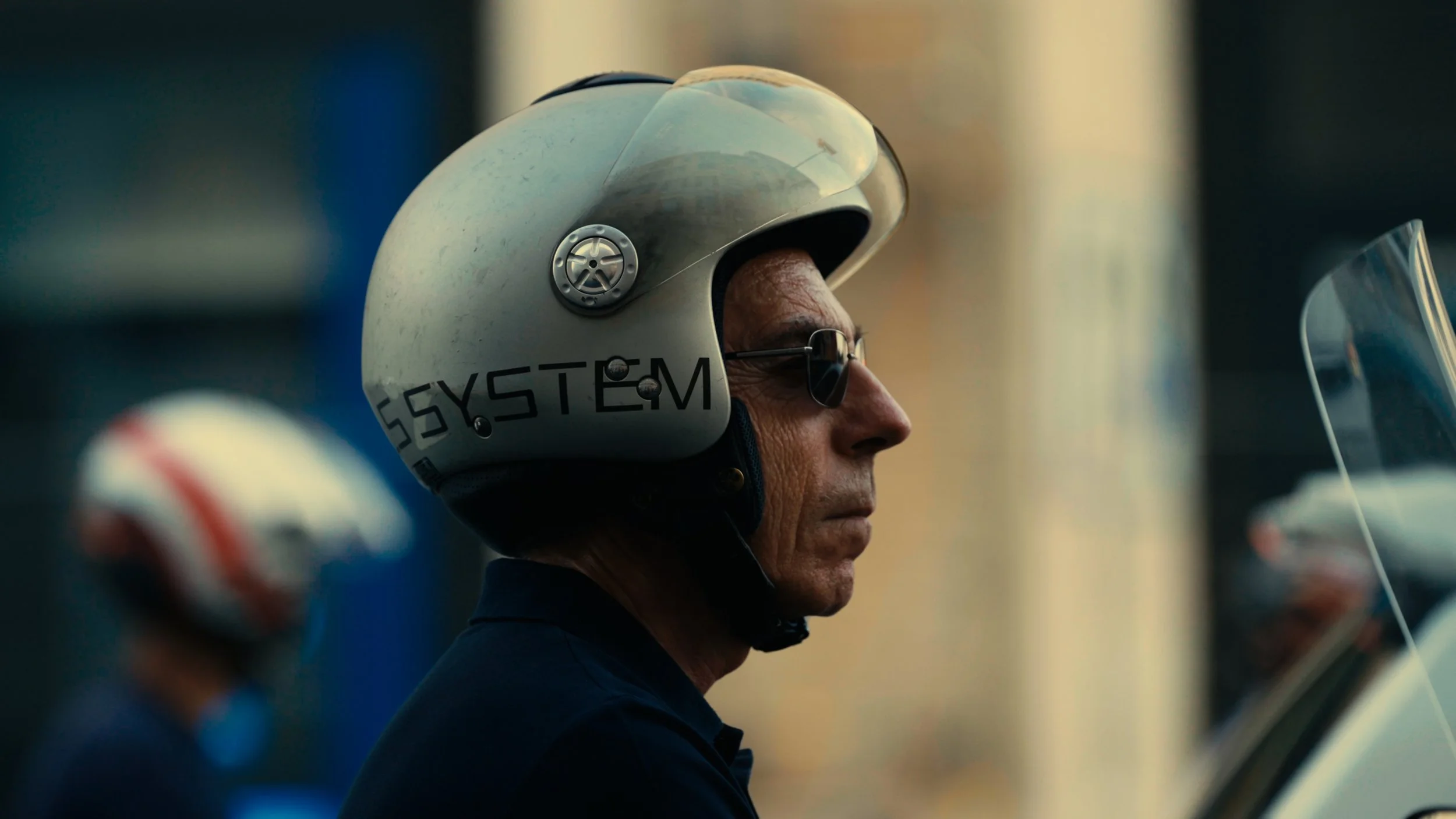 A man in profile wearing a white motorcycle helmet with black glasses and a black shirt, standing outdoors.