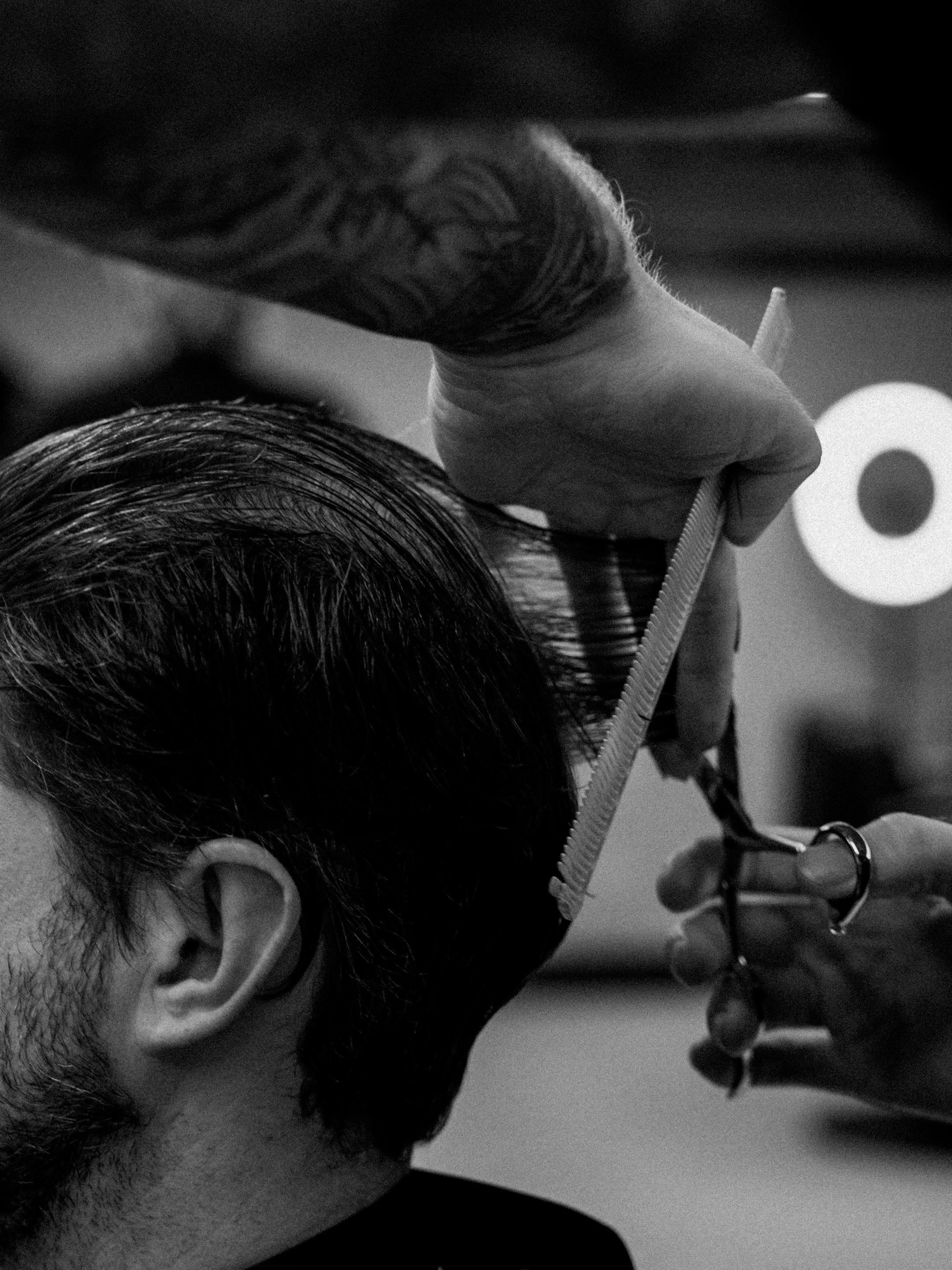 A person getting a haircut. The barber is using scissors and a comb to cut the client's hair.