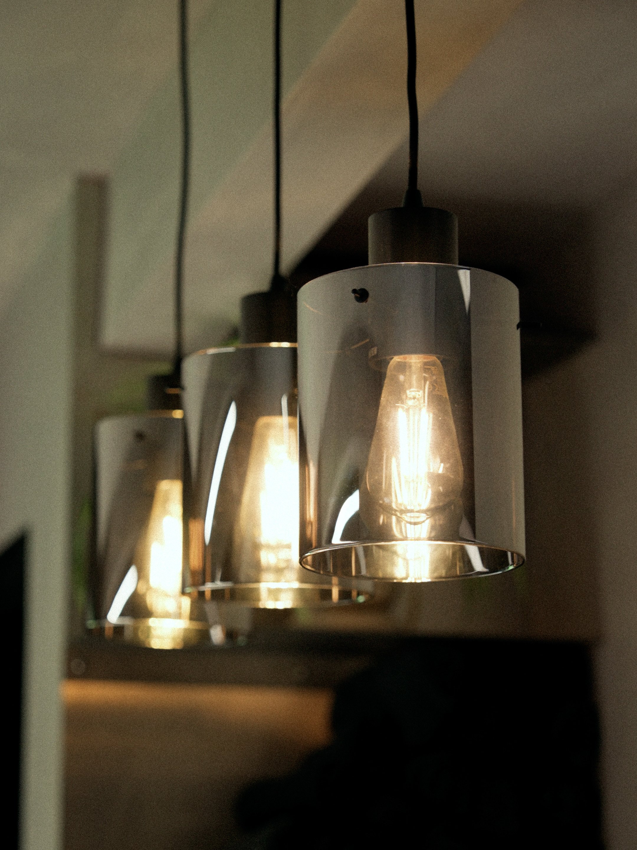 Three modern hanging pendant light fixtures with metallic shades and exposed bulbs, suspended from black cords.