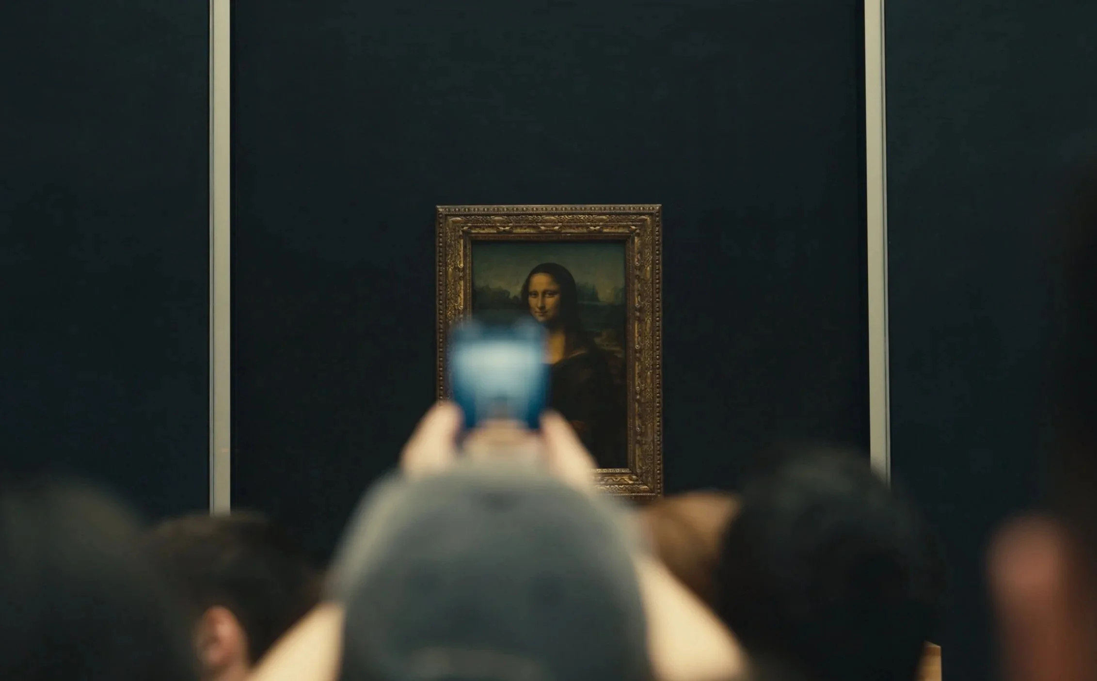 Visitors at the Louvre Museum in Paris taking a photo of the Mona Lisa painting.
