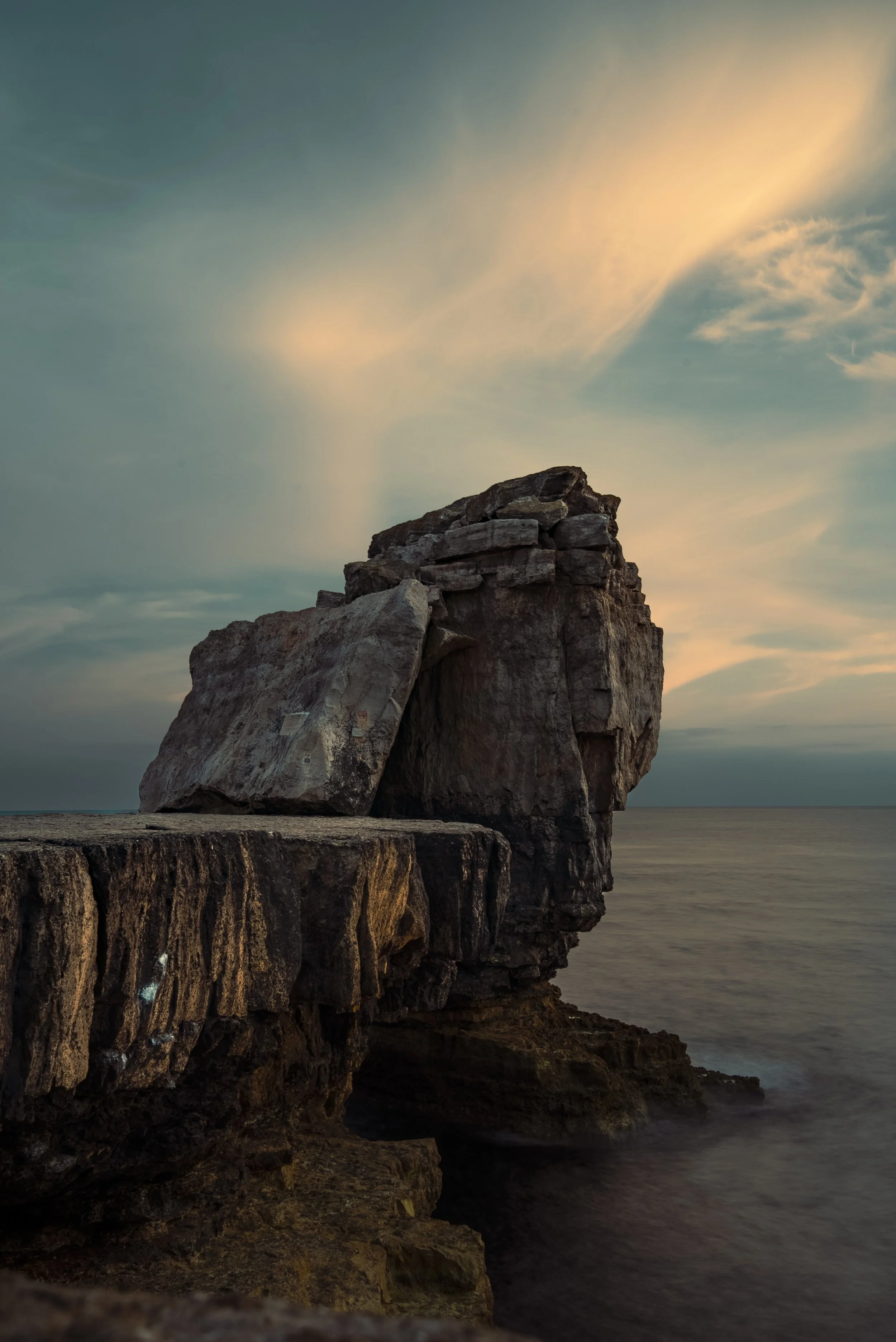 Large rock formation on the shoreline at sunset with a cloudy sky