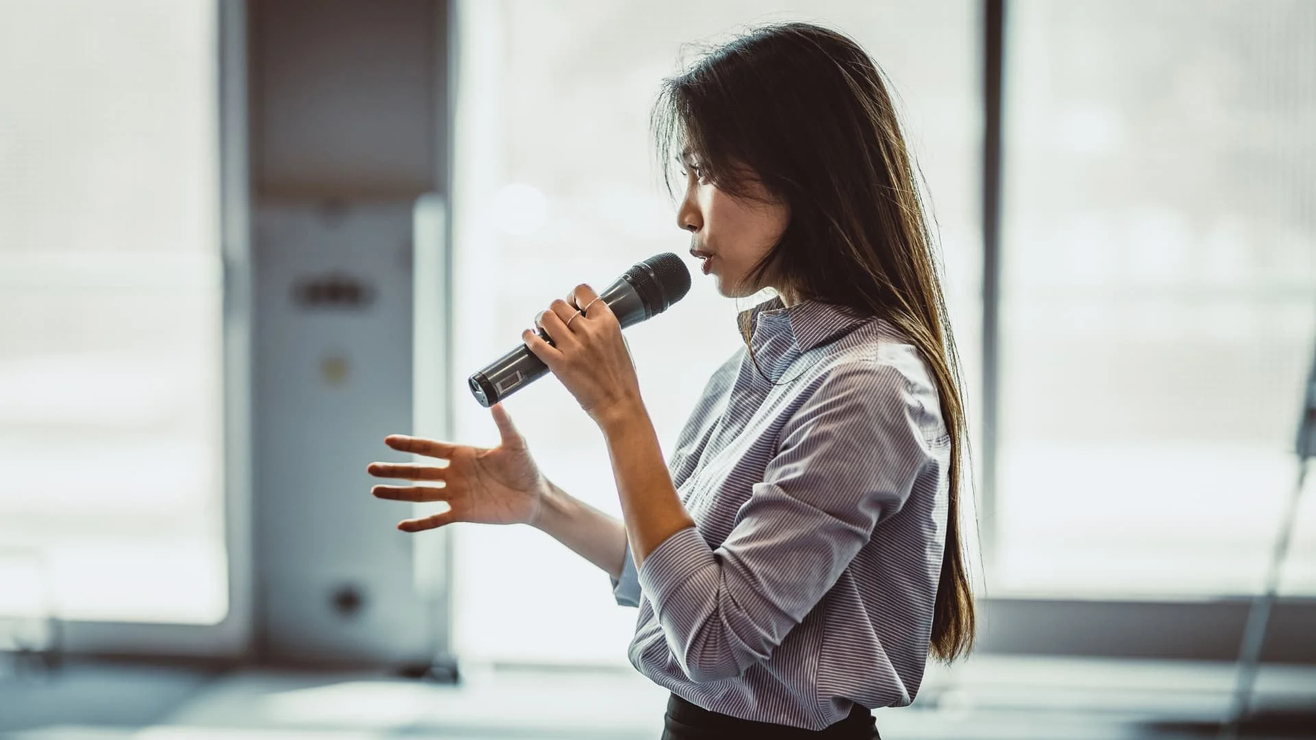 Professionally dressed woman holds a microphone while talking.