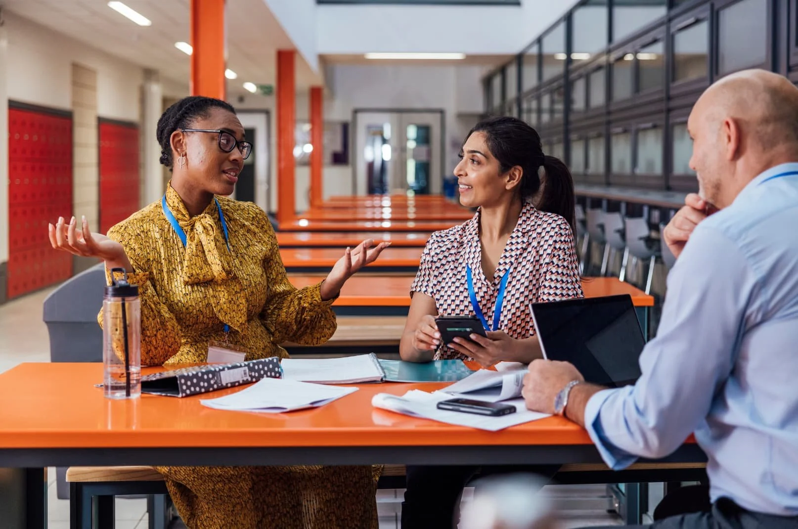 Three educators collaborating at a table in a school building, with papers and a tablet in front of them.