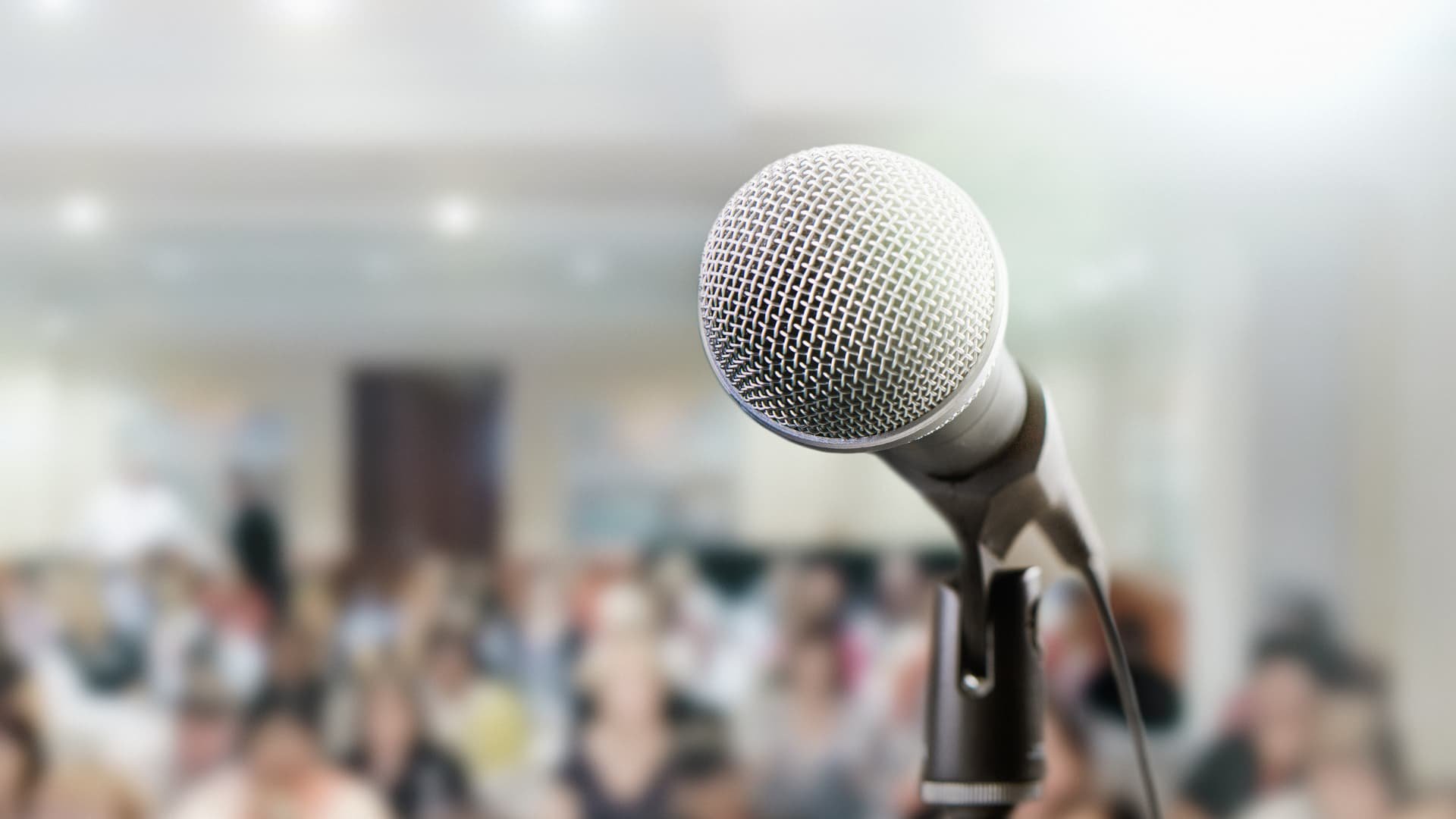 Microphone in focus with blurred background of people sitting, facing the microphone.
