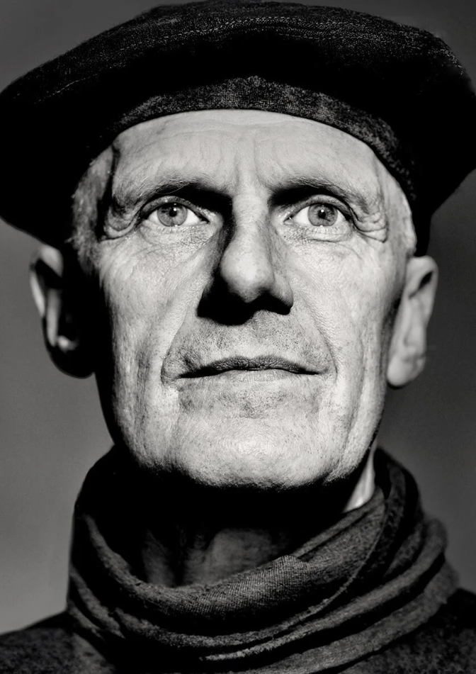 Black and white portrait of sculpture Tim Pomeroy wearing a dark beret and scarf, looking directly at the camera.