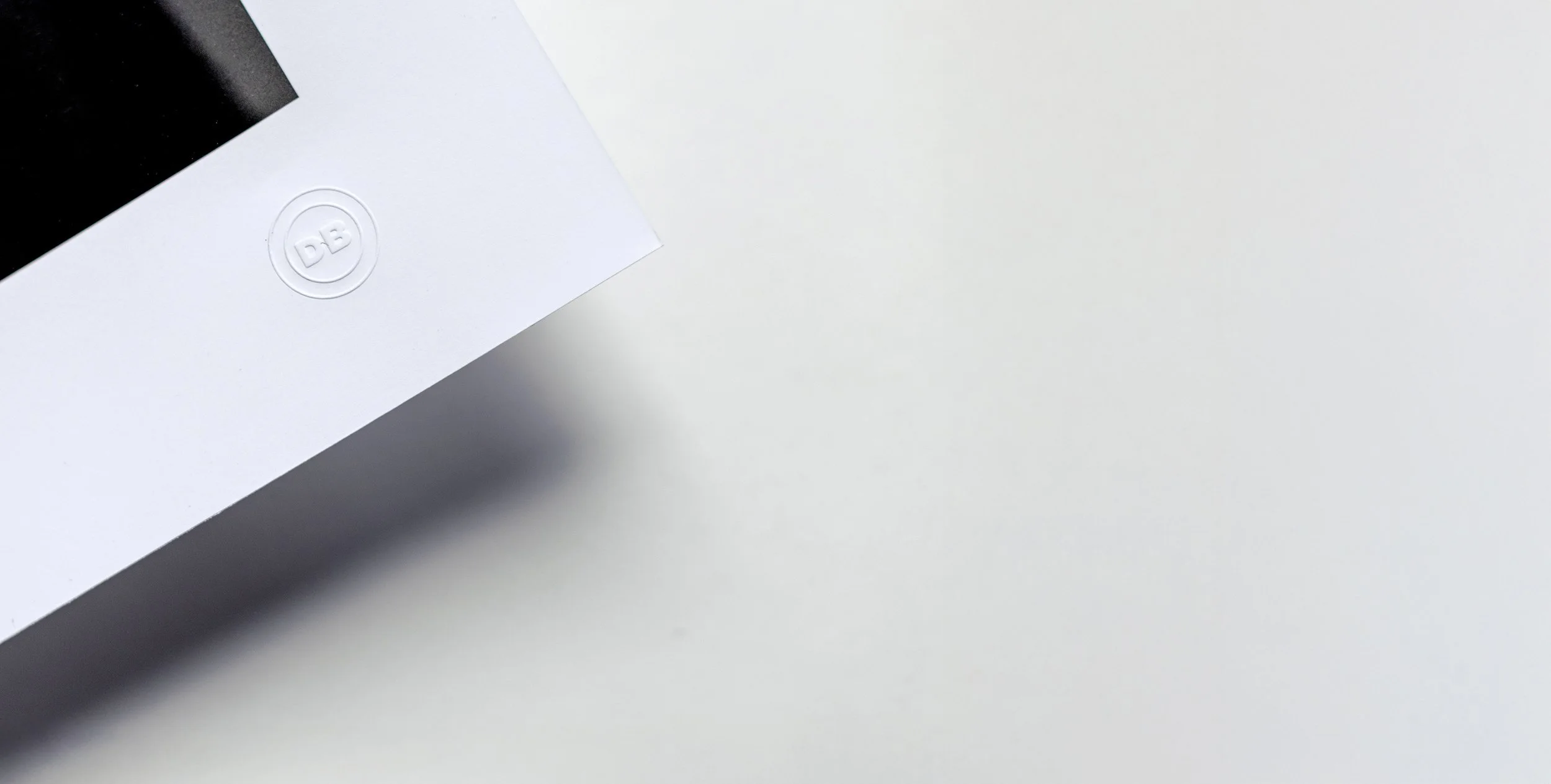 Close-up of a corner of a white box with a circular logo embossed with the letters 'DB' on a light surface.