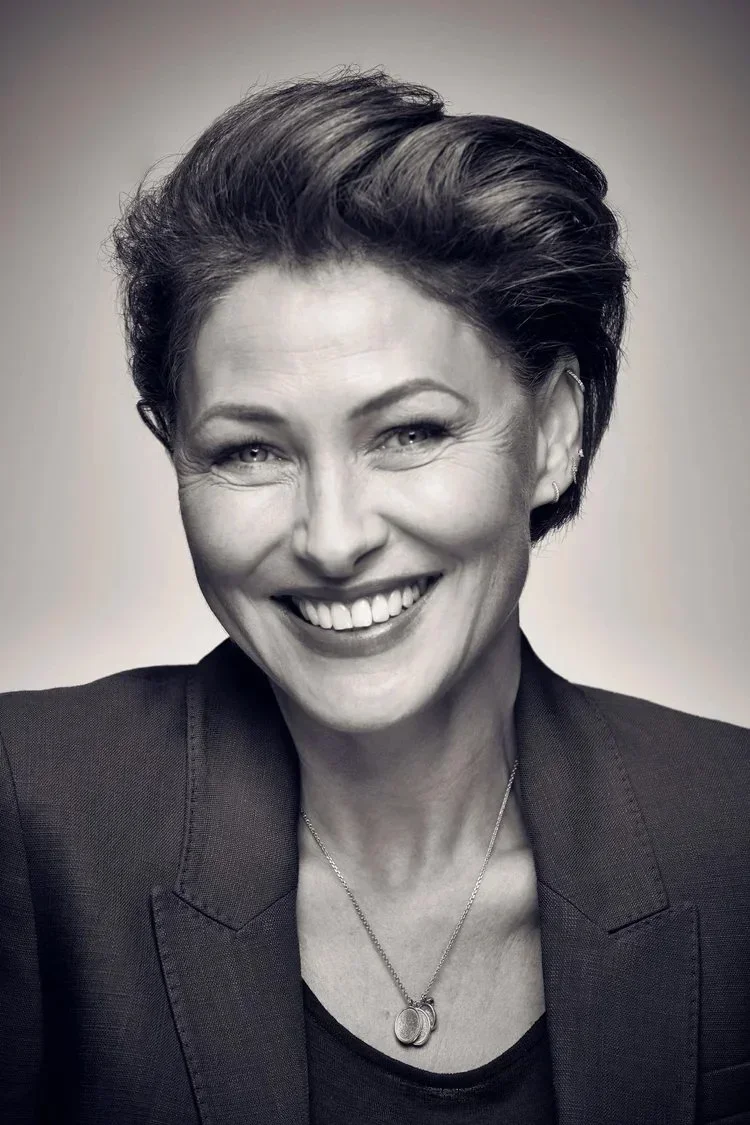 Black and white portrait of a smiling woman with short hair, wearing a blazer and a necklace.