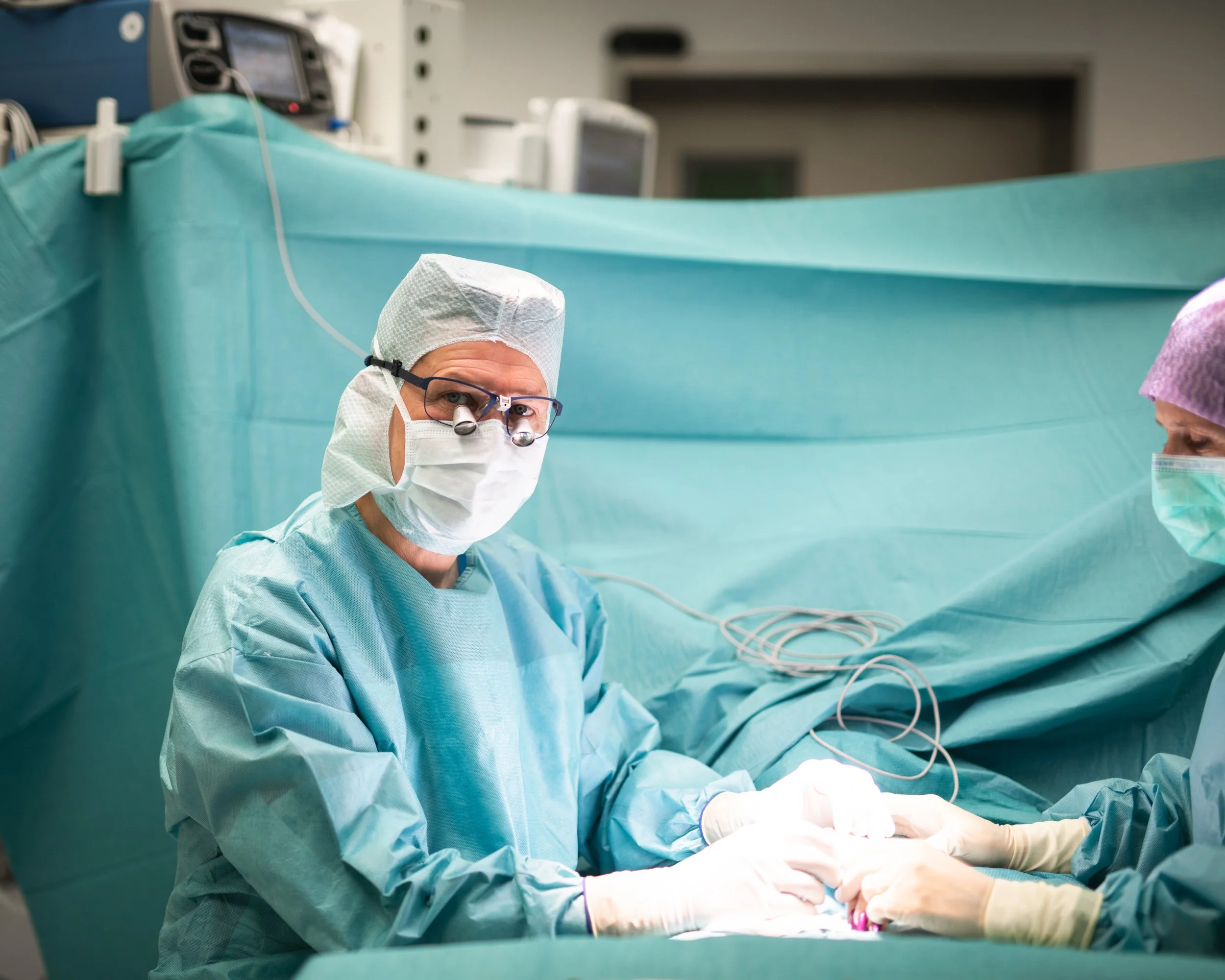 Ärzte und Pflegepersonal während einer Operation im Operationssaal, alle tragen Schutzkleidung, Masken und Kappen.