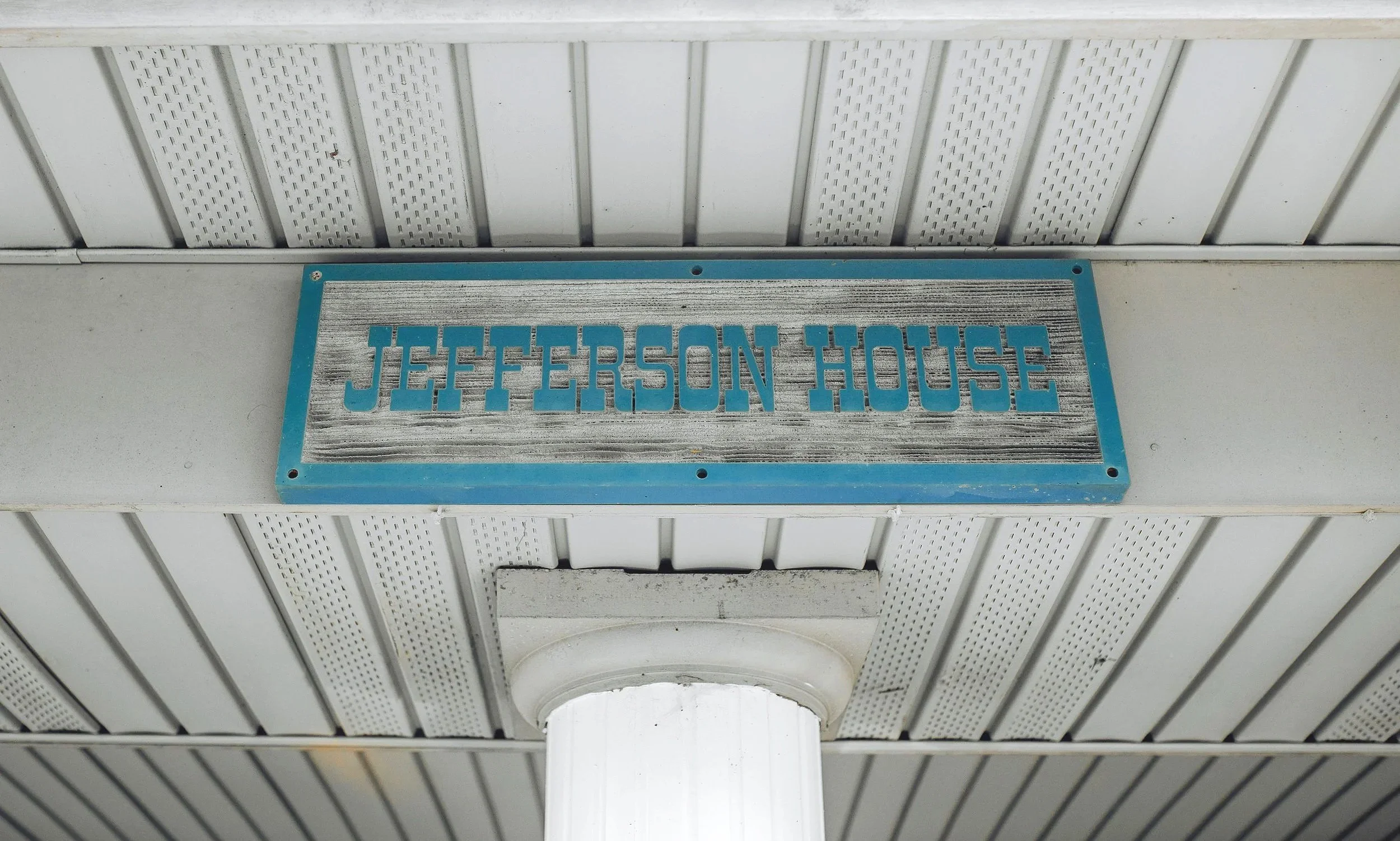 A sign that reads 'Jefferson House' mounted on a white beam underneath a white ceiling with perforated panels.