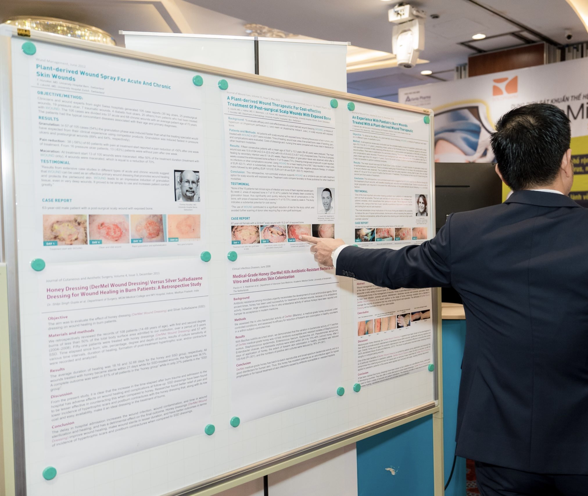 A man in a suit pointing at a scientific research poster displayed on a bulletin board at a conference or academic event.