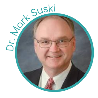 A professional headshot of a middle-aged man with glasses, wearing a suit and tie, smiling at the camera.