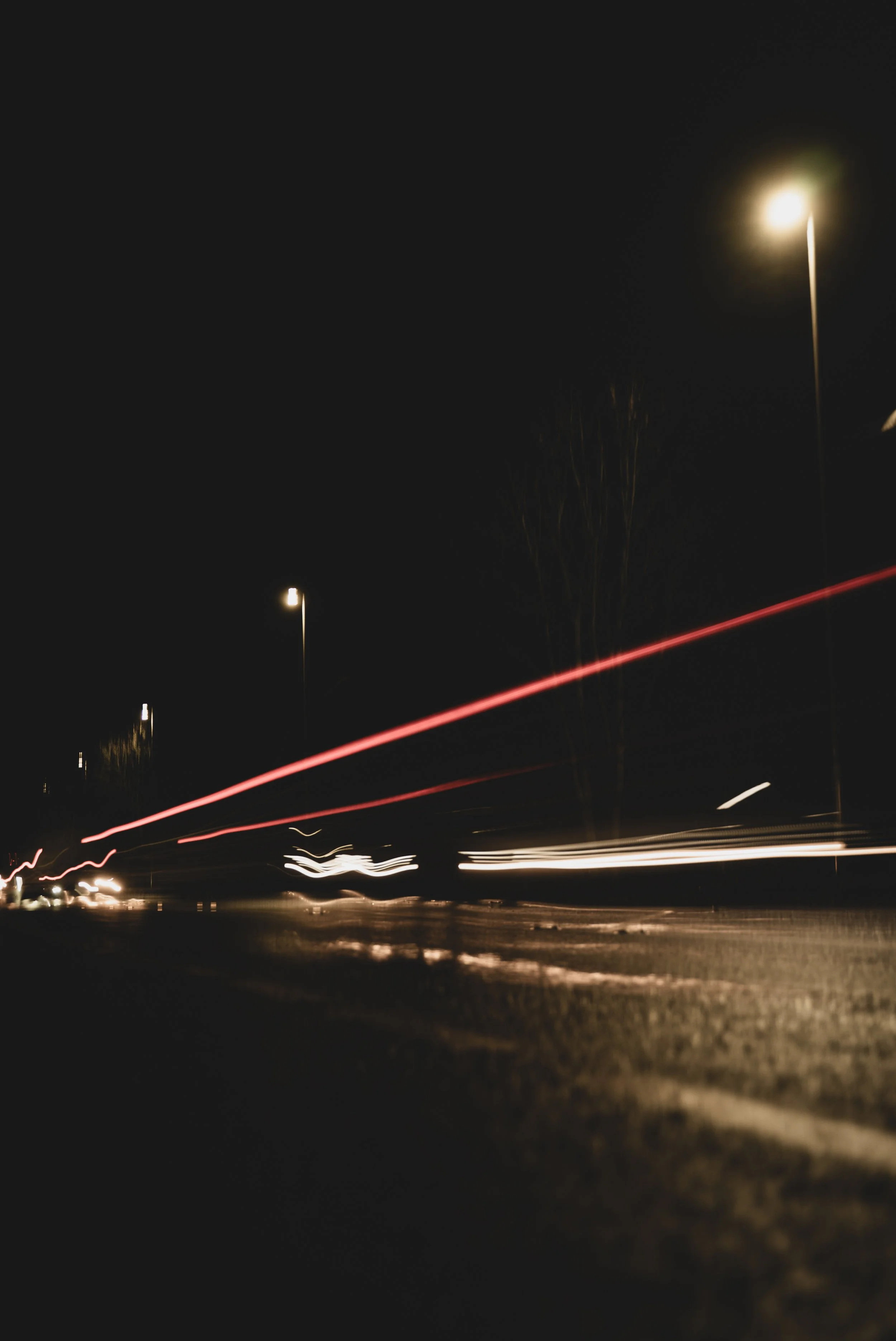 Long exposure photograph capturing light trails from moving vehicles on a dark street at night, with streetlights illuminating the scene.