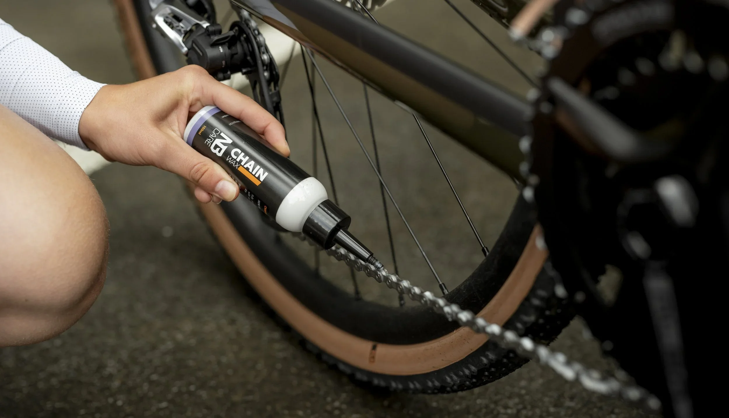 Persoon smeert kettingwax op de ketting van een mountainbike.