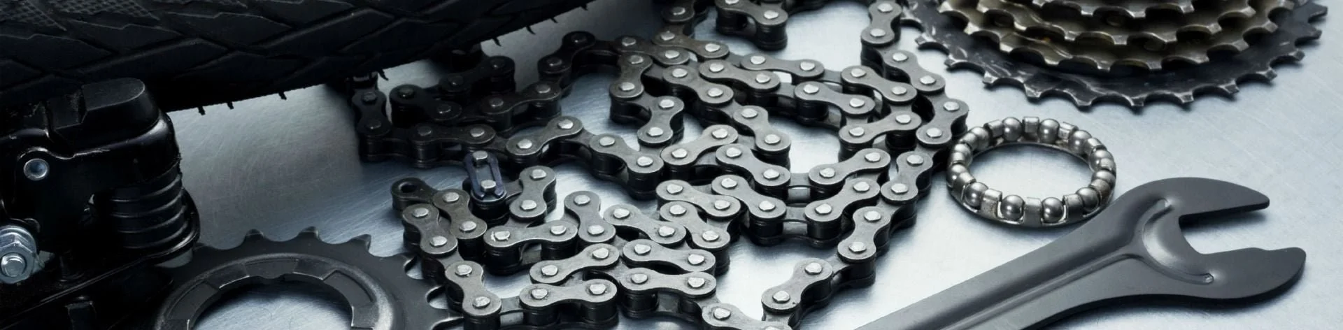 Diverse machineonderdelen, zoals kettingen, een ringen en een moersleutel, uitgestald op een metalen oppervlak.