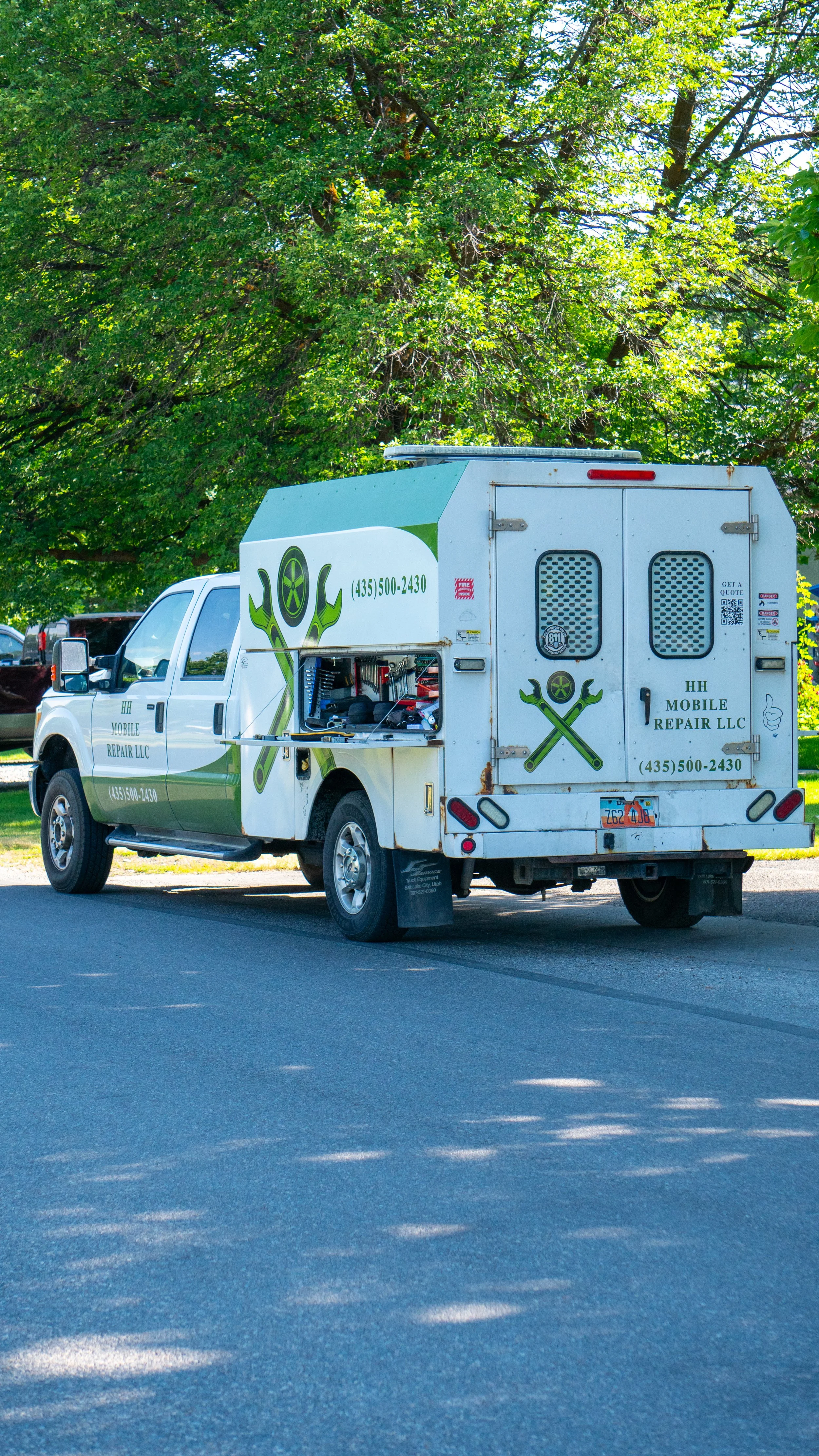 Service utility truck for mobile repair LLC parked on a street under large green trees.