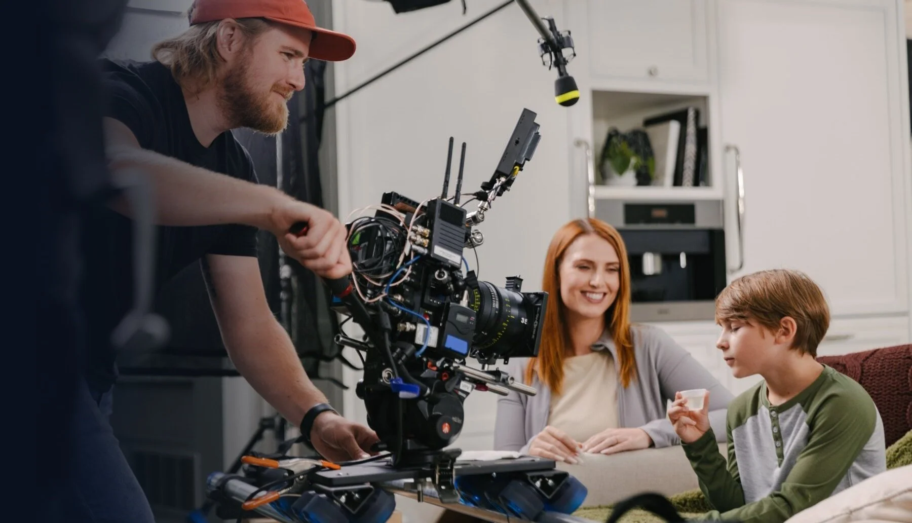 Filmmaker operating camera while woman and boy sit on couch in living room.