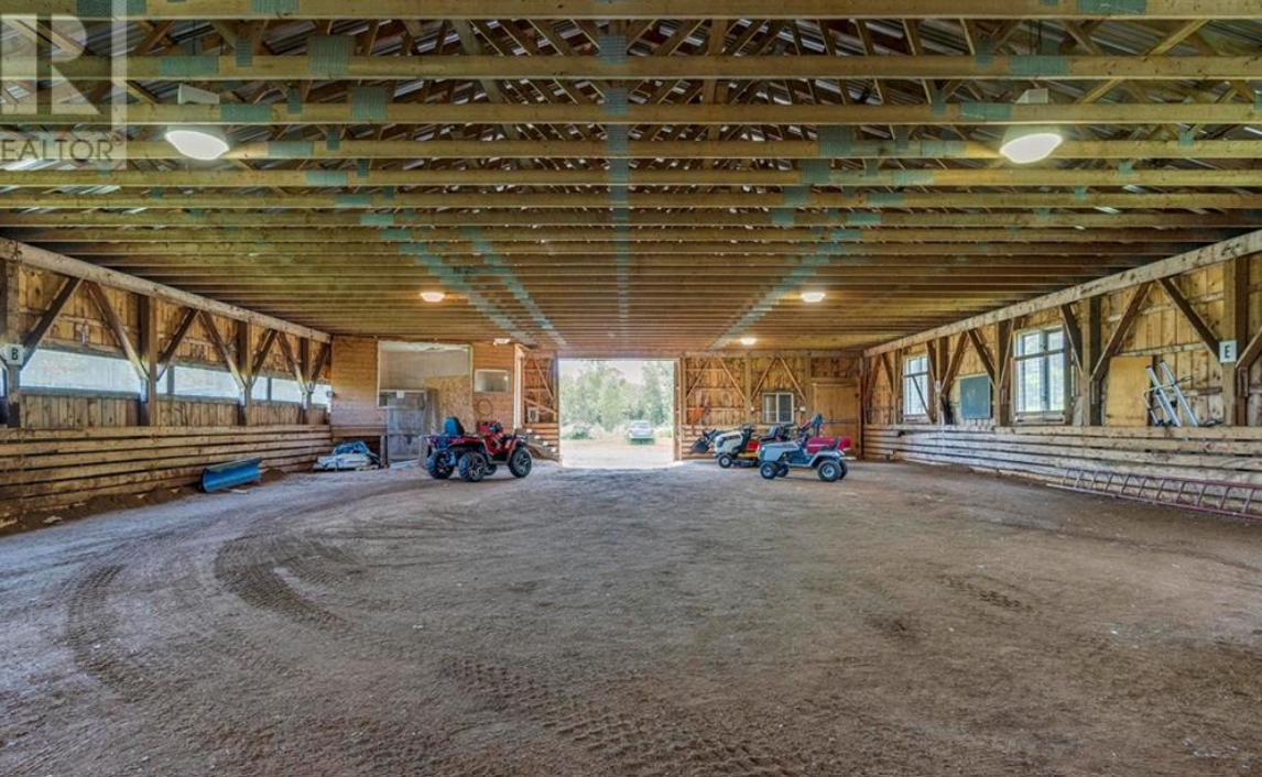 Empty indoor barn with dirt floor, small toy vehicles, and a large open entrance showing outdoor trees and sky.