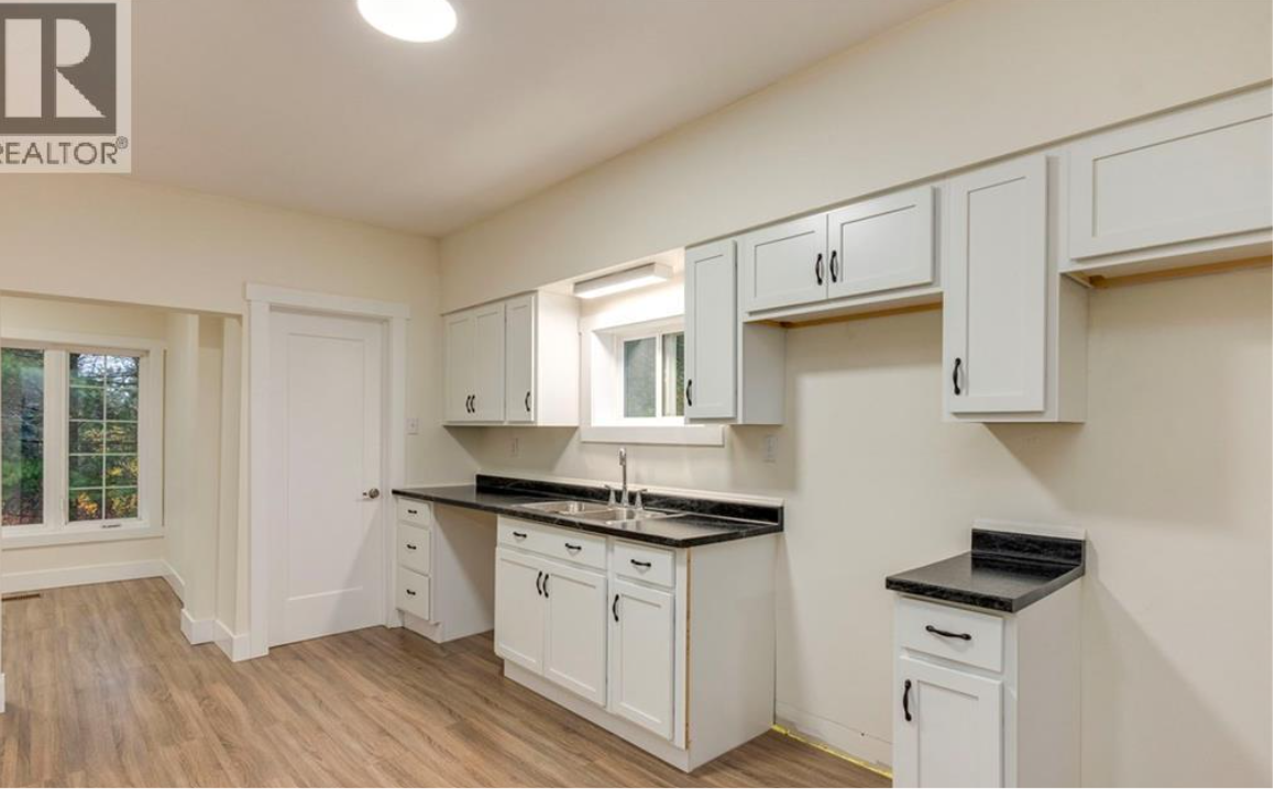 Kitchen with white cabinets, black countertops, a window above the sink, and a door leading to another room.
