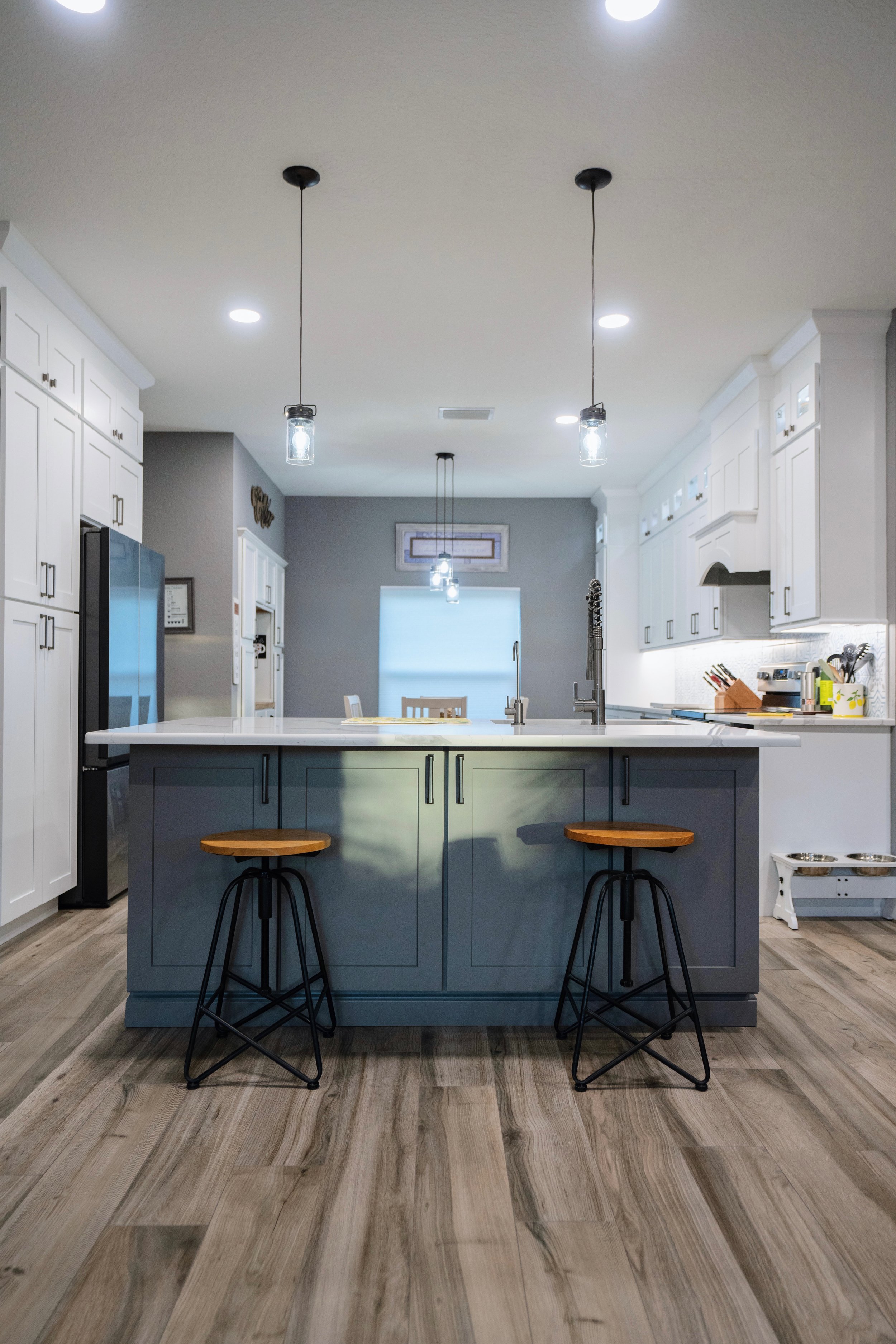 Modern kitchen with a gray island, white cabinetry, pendant and recessed lighting, and wooden floor.