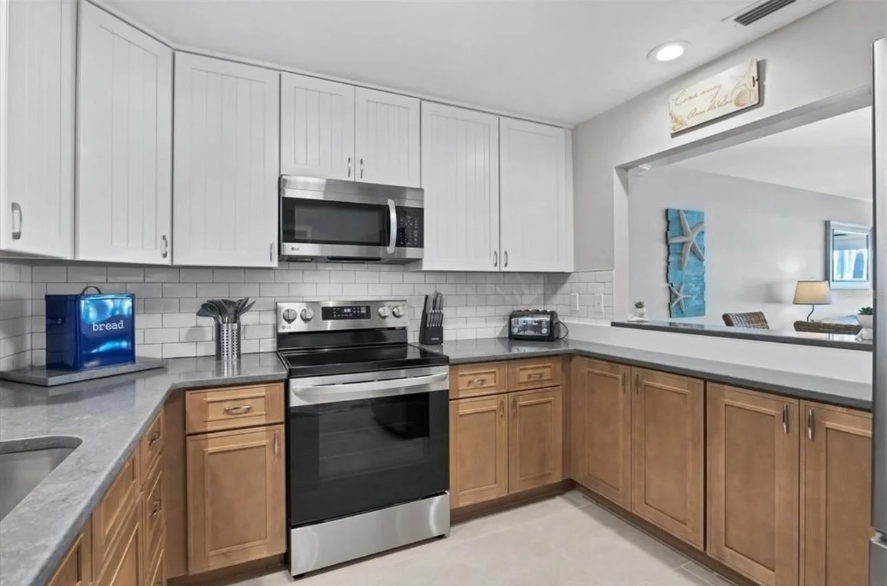 Kitchen with white upper cabinets, wooden lower cabinets, stainless steel microwave and oven, gray countertops, and a white subway tile backsplash.