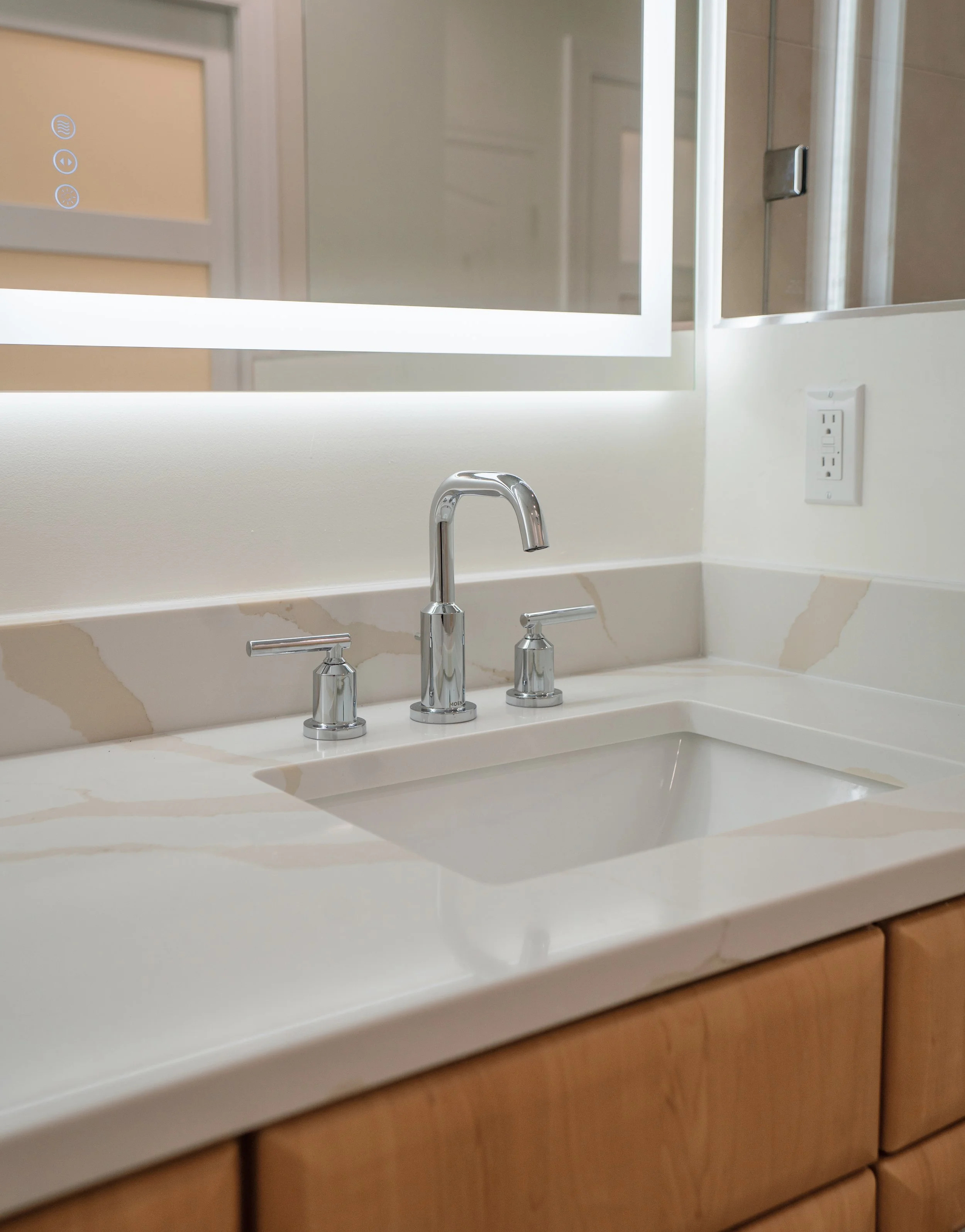 Bathroom sink with a chrome faucet and two handles, and a mirror above the sink, in a well-lit bathroom.