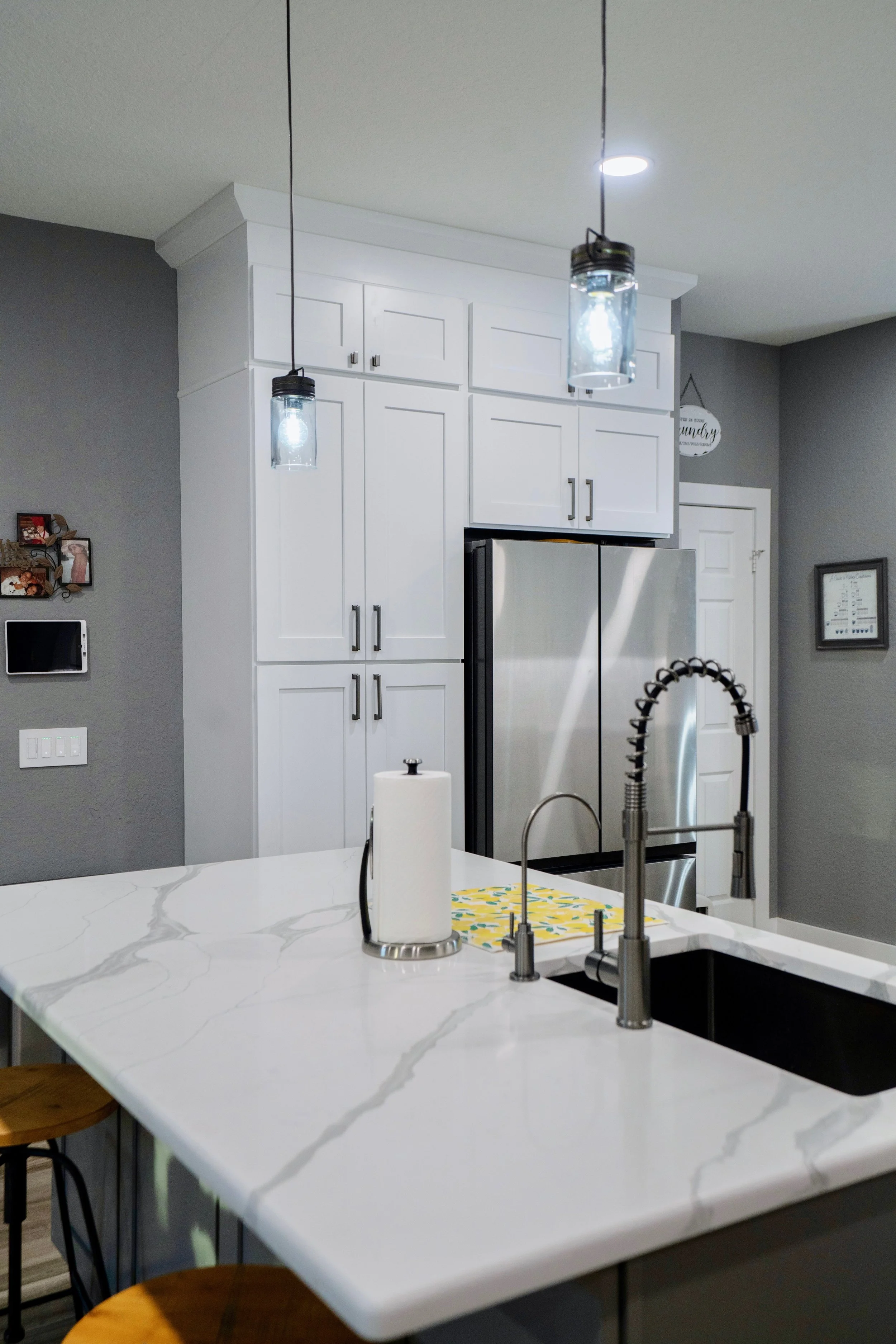 Modern kitchen with white cabinets, stainless steel refrigerator, marble island, and hanging pendant lights.