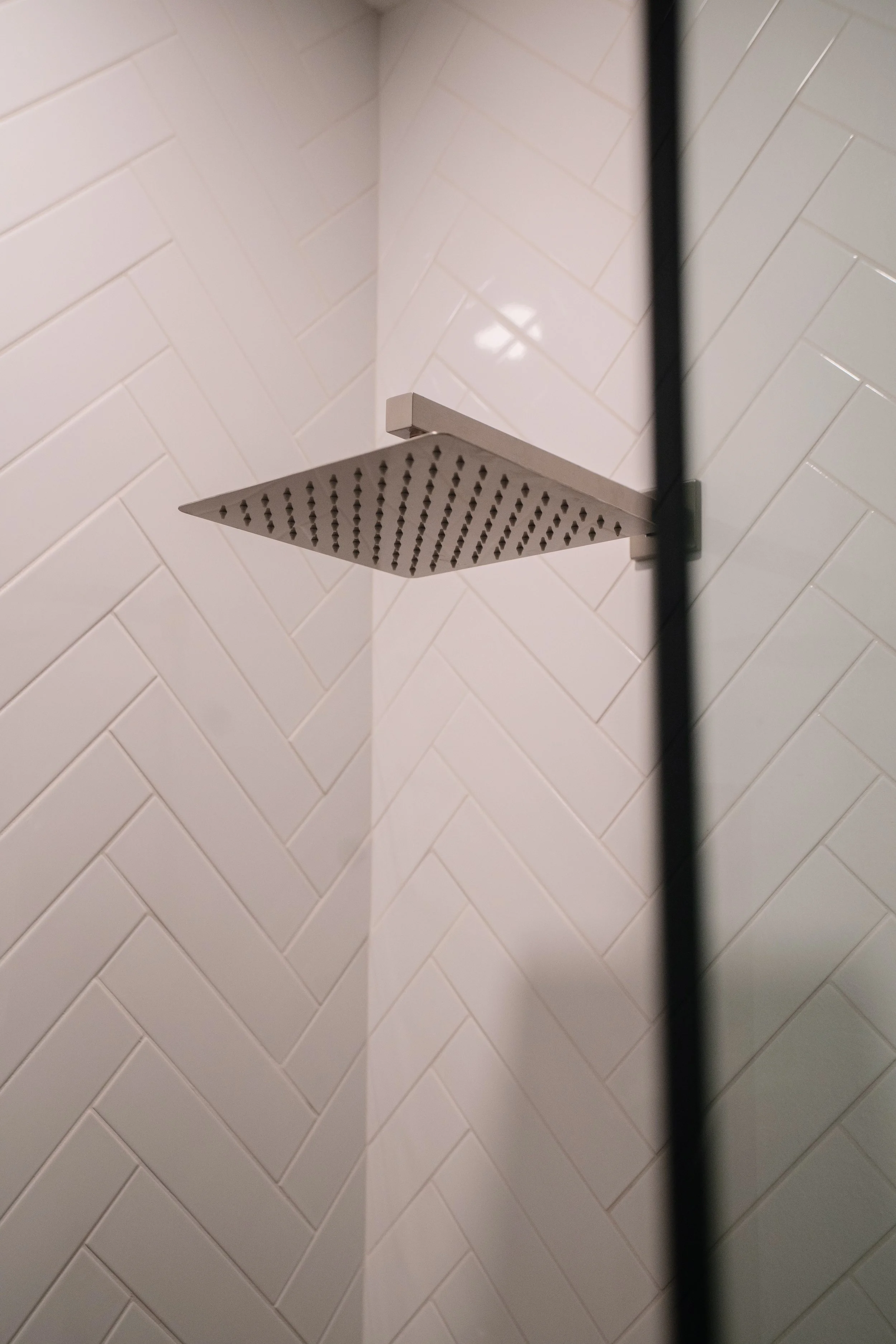 Close-up of a square, rain showerhead mounted on a tiled wall in a shower.