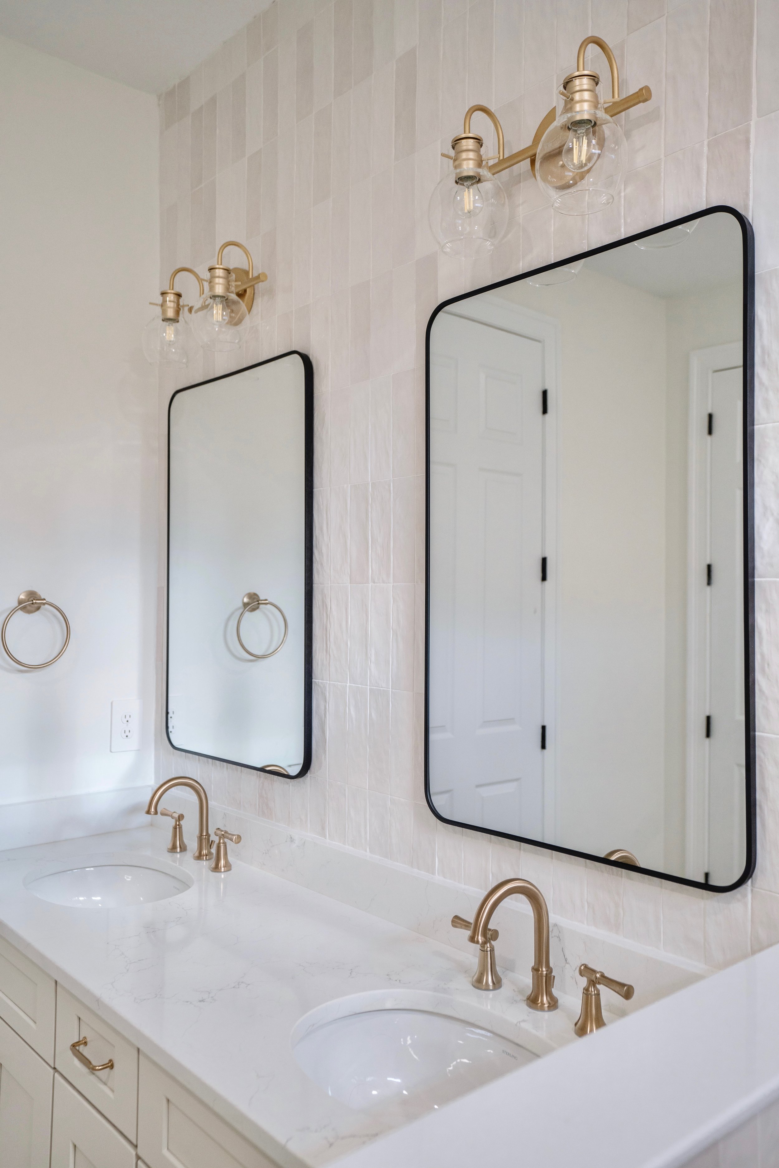 Double bathroom vanity with two mirrors, two gold faucets, and two light fixtures.