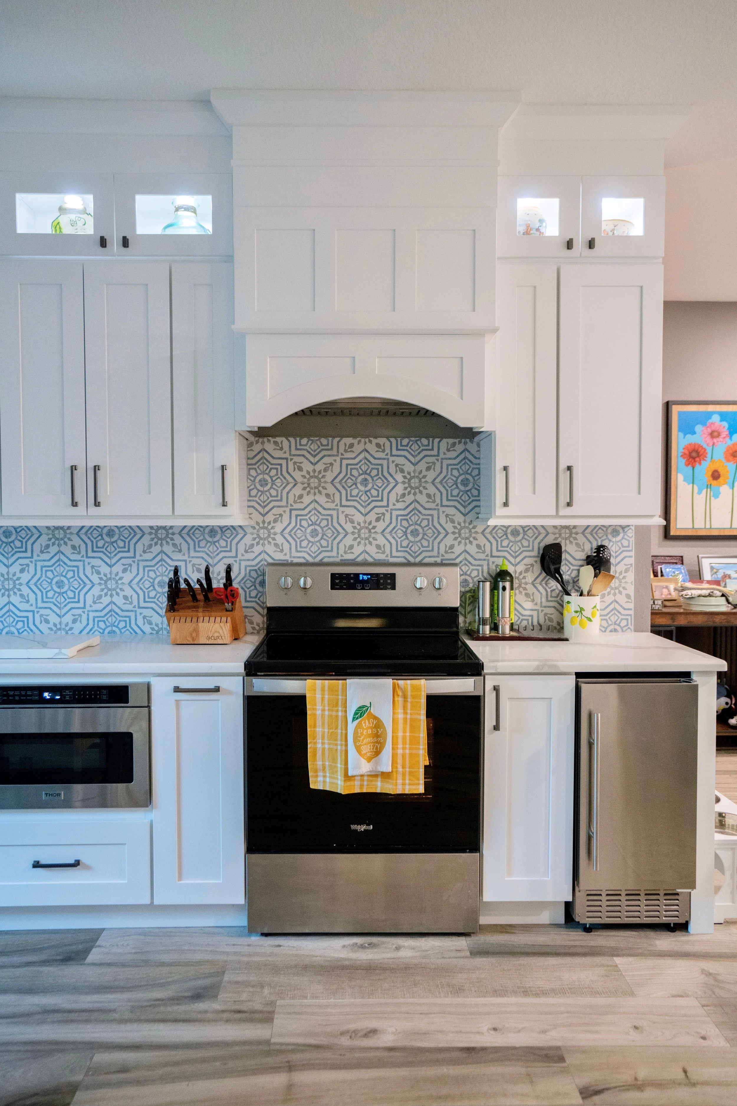 Kitchen with white cabinets, patterned backsplash, stainless steel stove, and various kitchen utensils and appliances.
