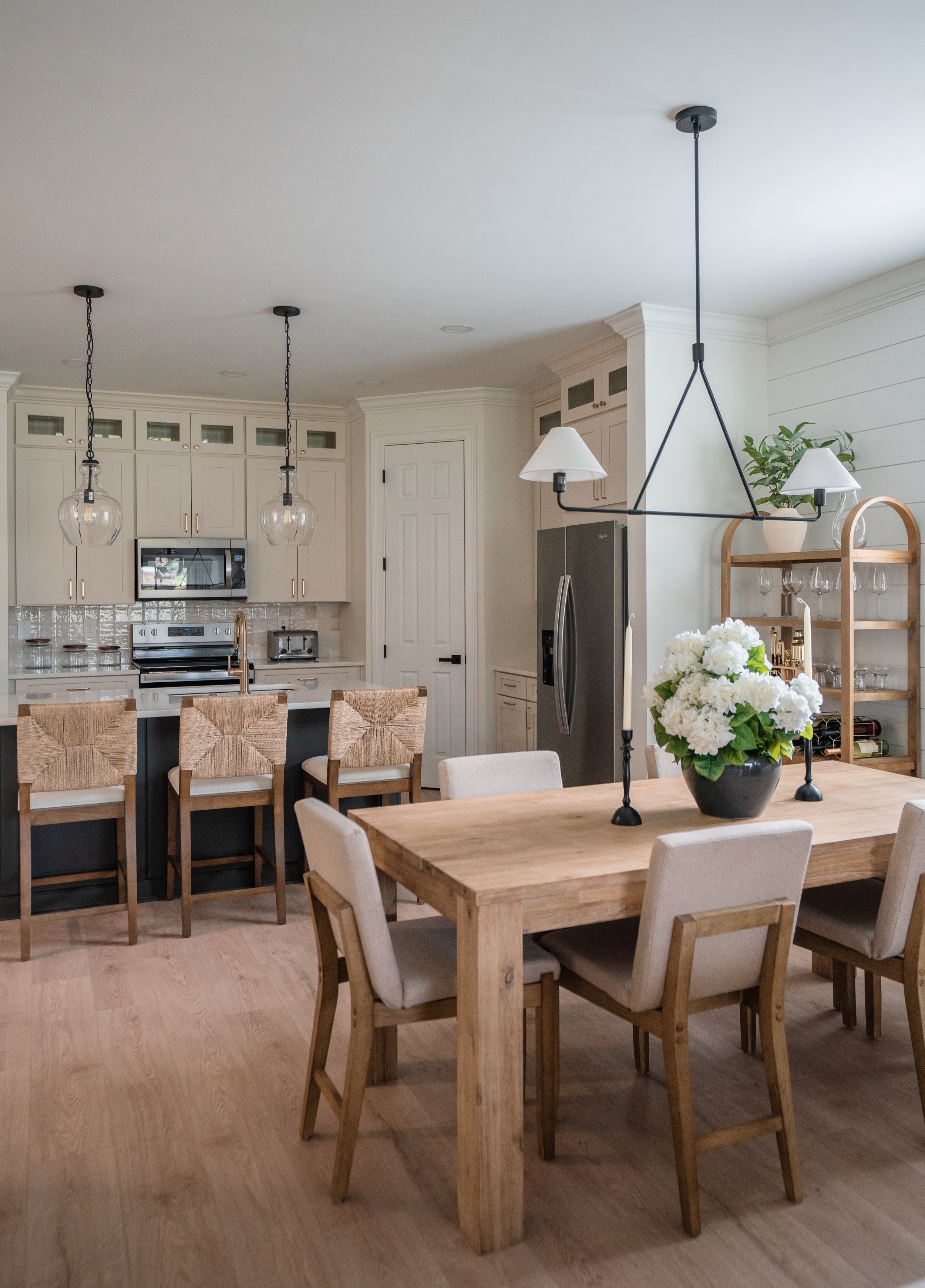 Open-concept kitchen and dining area with a wooden table, white chairs, a vase of white flowers, and modern light fixtures.