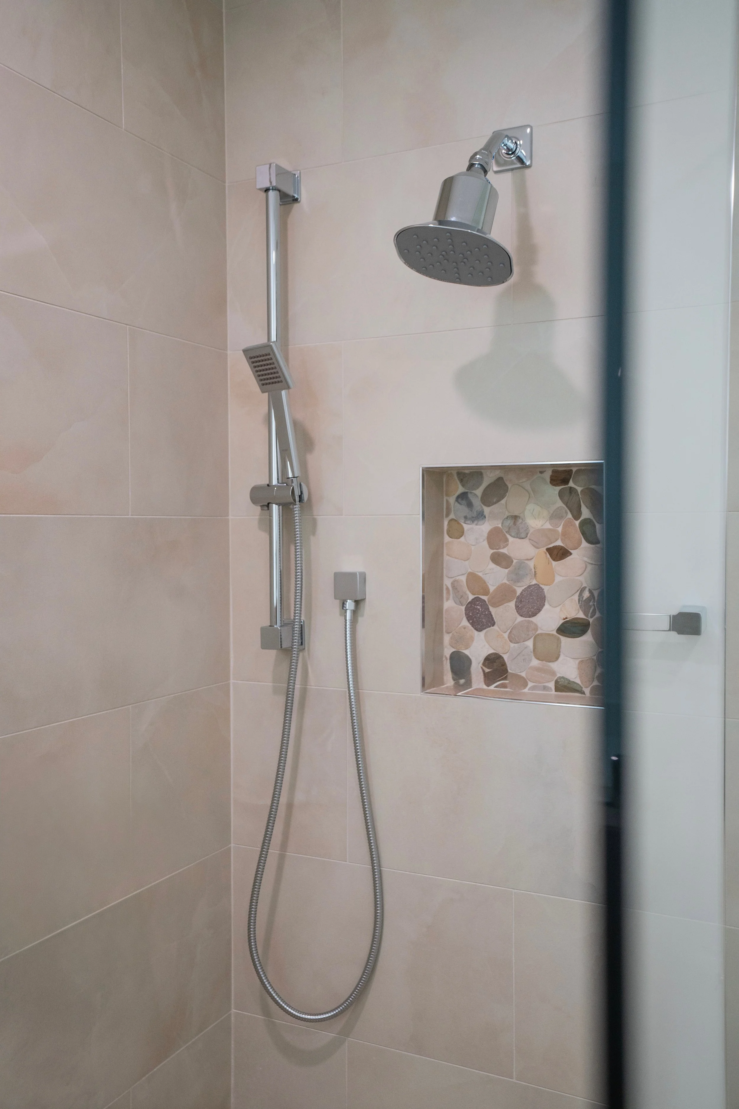A showerhead with a hand-held attachment and pebble tile accent in a walk-in shower.