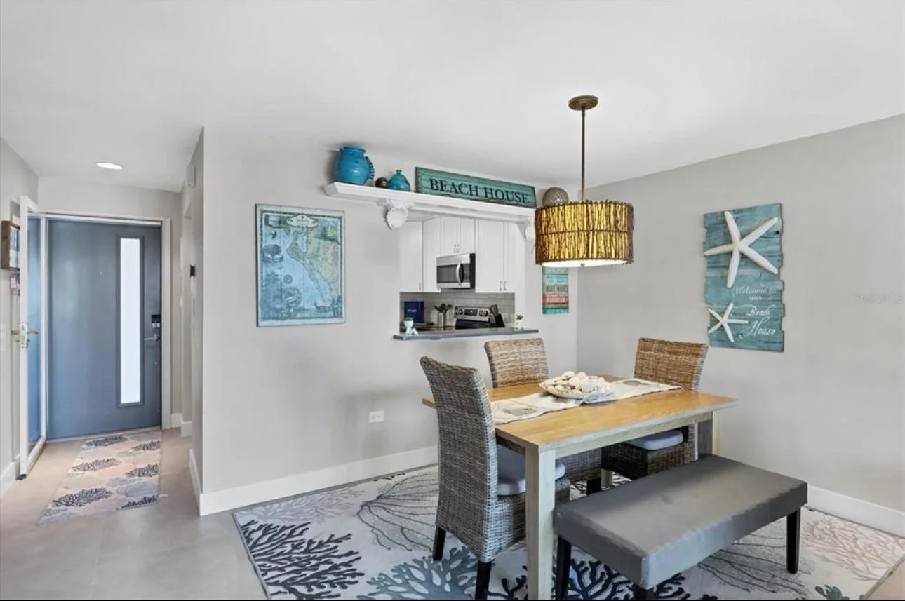 Coastal style dining area with a light wood table, wicker chairs, decorative sea-themed wall art, and beach-themed decor including starfish and shells.