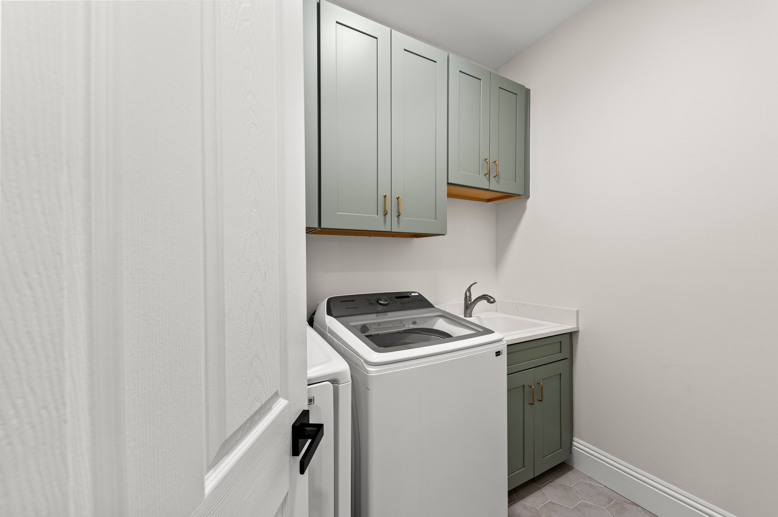 Laundry room with green wall cabinets, a washing machine, a utility sink, and tiled flooring.