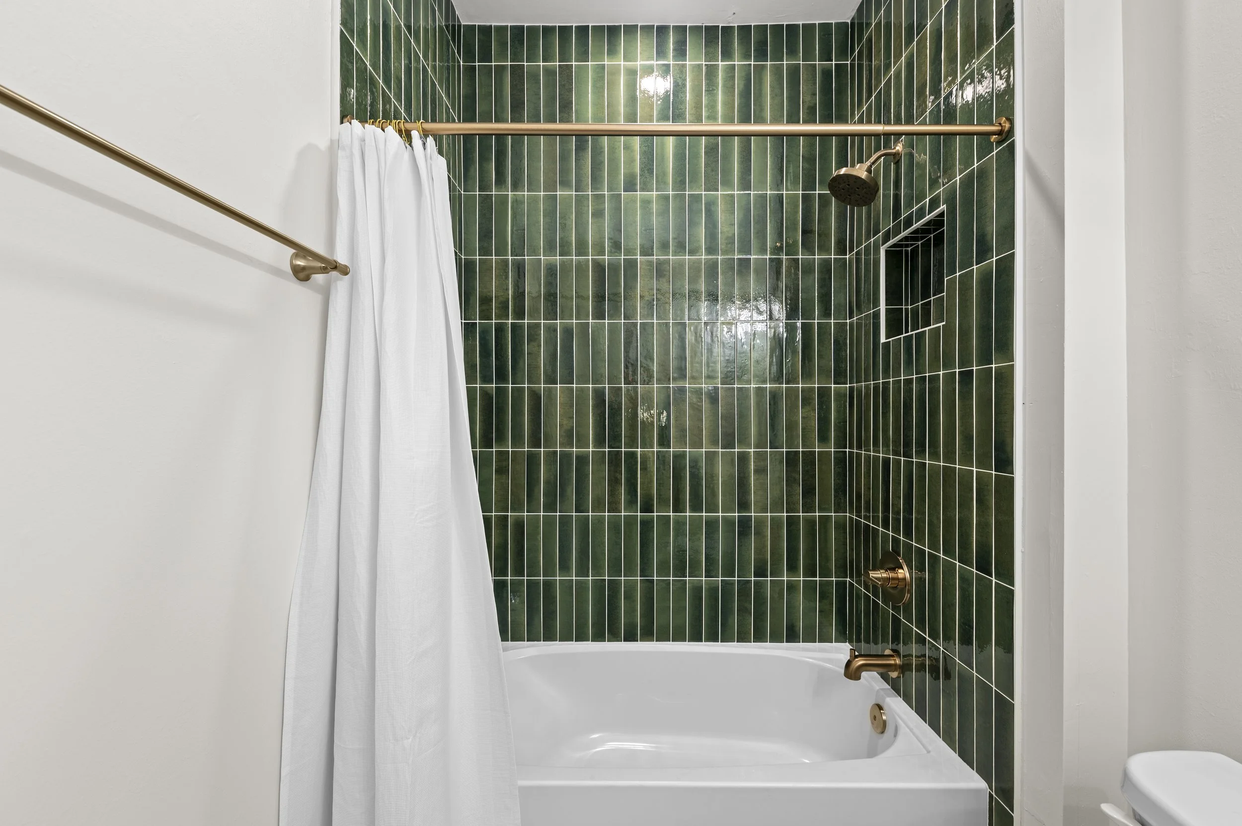 Bathroom with a bathtub, green tiled wall, and white shower curtain.