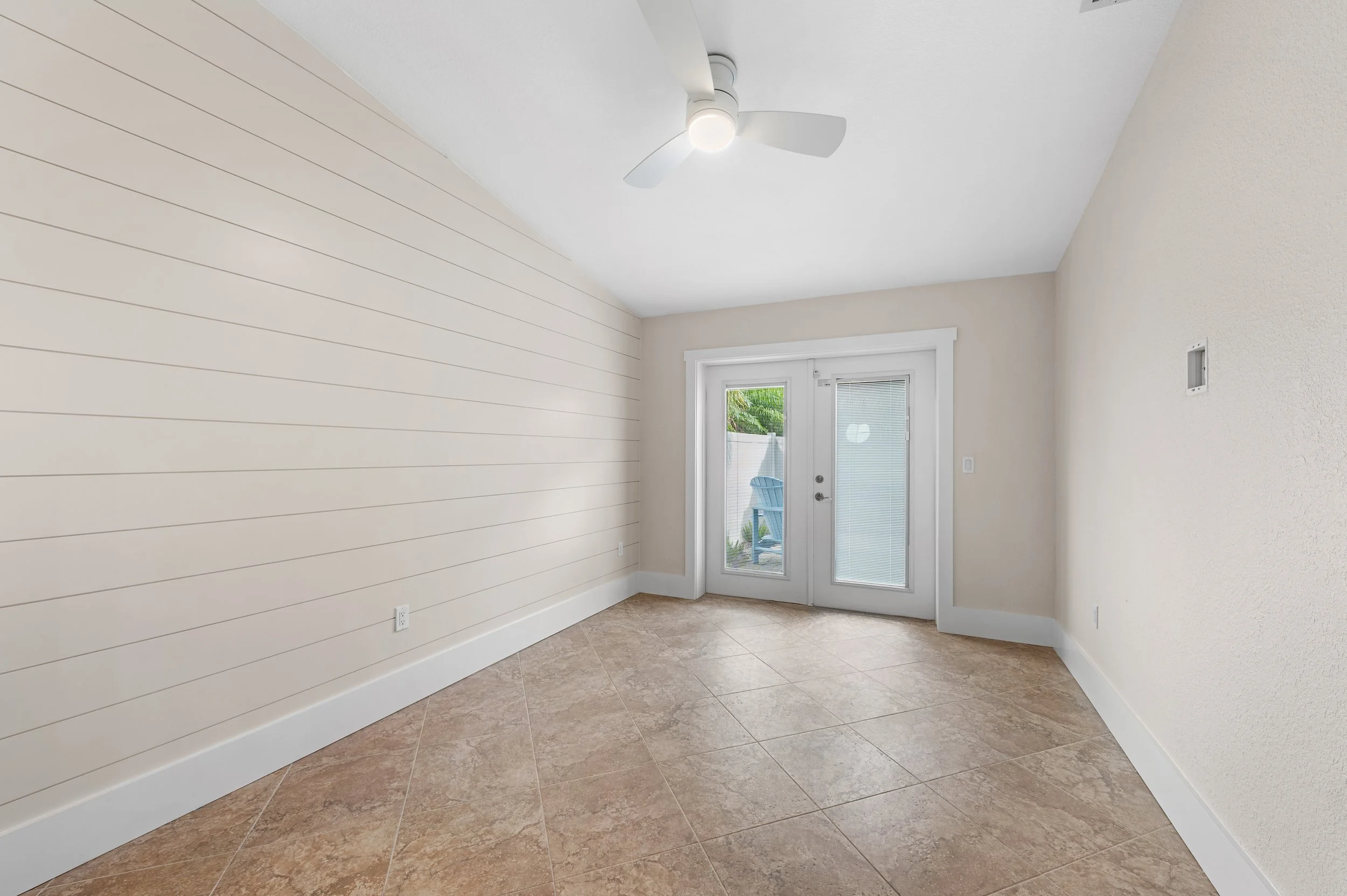 Empty room with beige tile flooring, white walls, a sliding door with glass panels leading outside, and a ceiling fan with light.